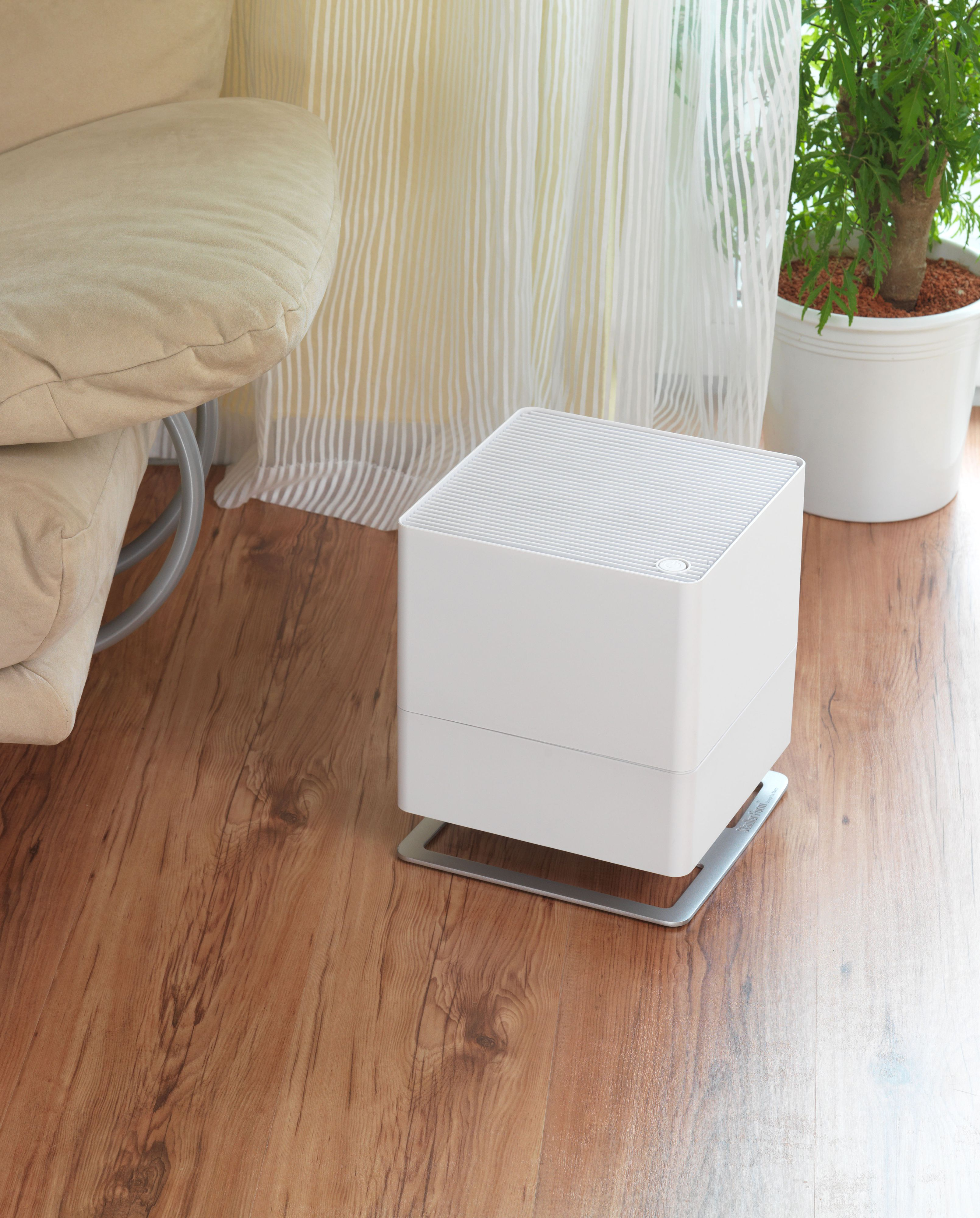 White air purifier on wooden floor, with sofa and plant.
