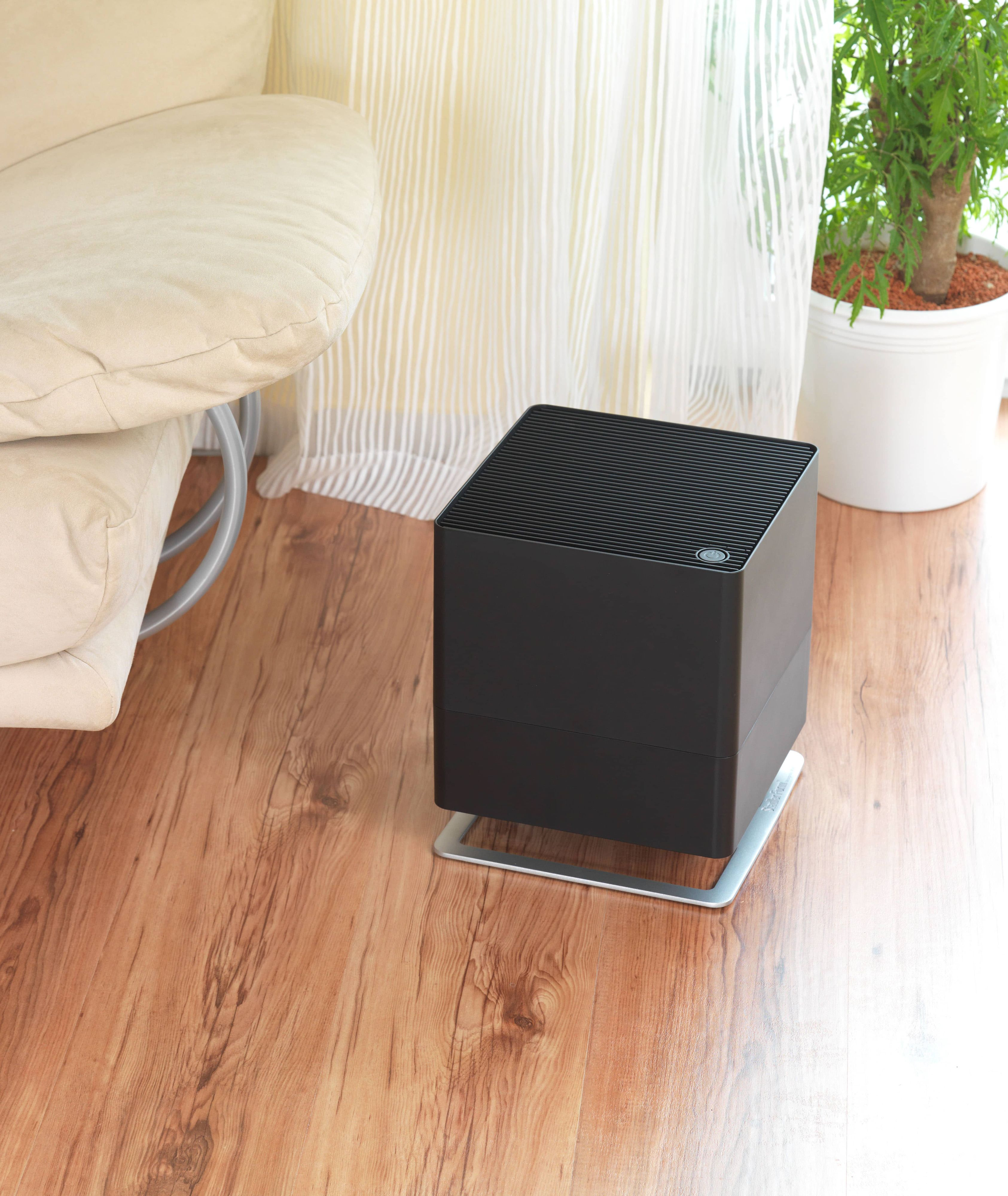 Black air purifier on wooden floor, with sofa and plant.