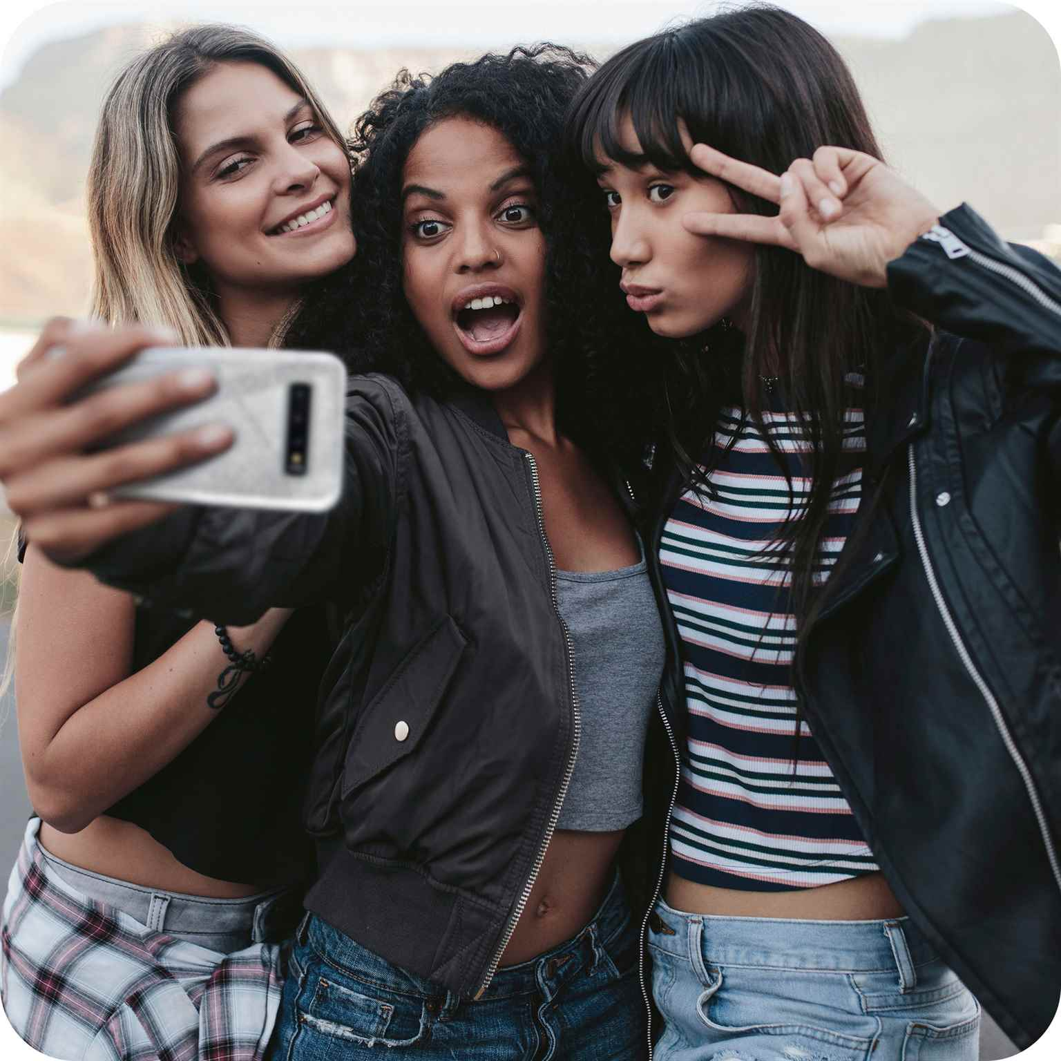 Drei Frauen machen ein Selfie mit einem Telefon. Eine lächelt, die anderen beiden posieren mit Ausdrücken.