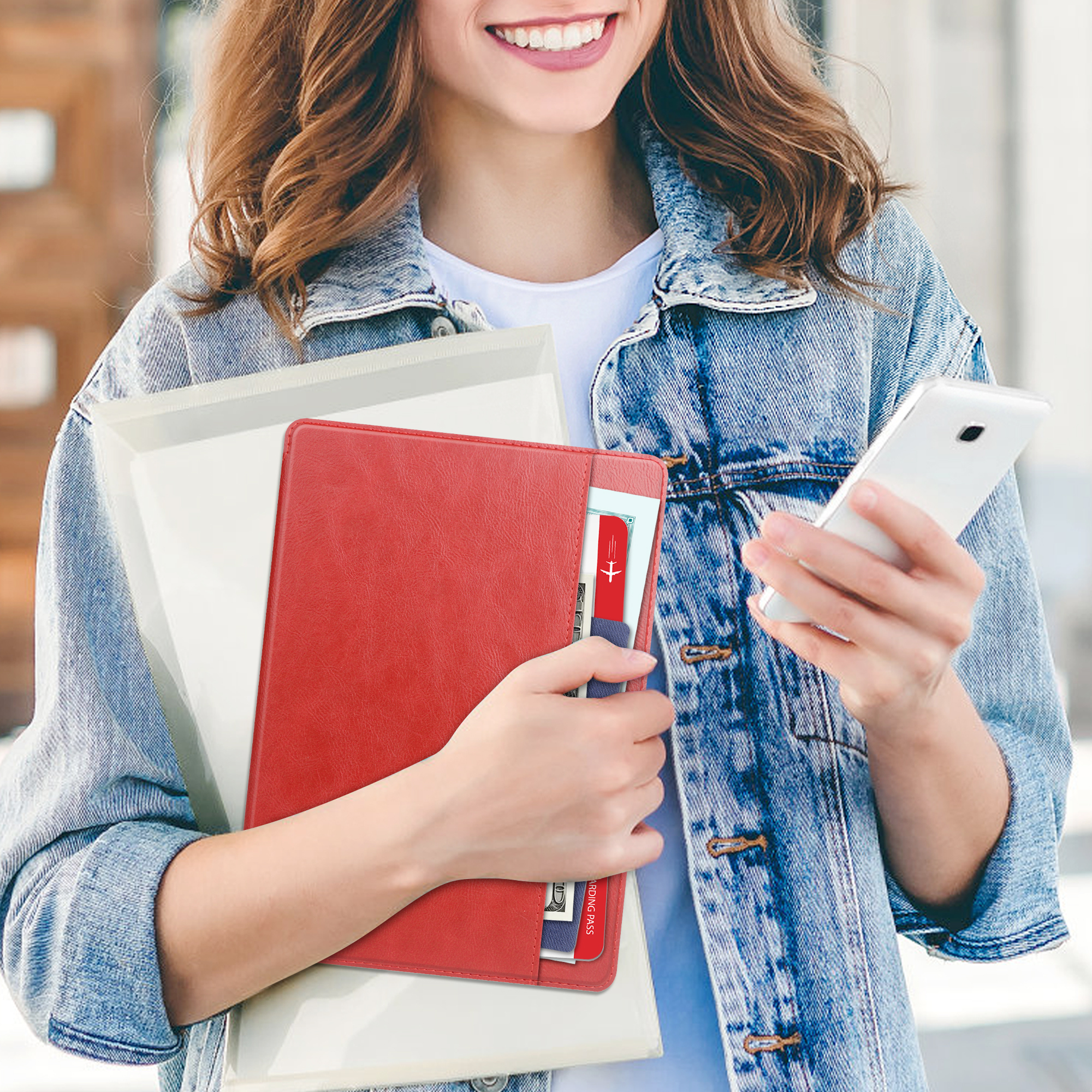 Frau hält ein rotes Notizbuch mit Karten. Sie ist draußen und trägt eine Jeansjacke.