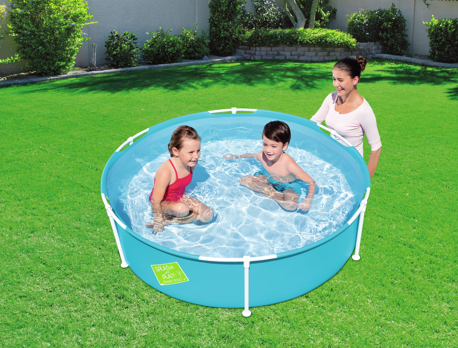 Kinder in einem blauen Pool mit einem Erwachsenen auf einer grünen Wiese.
