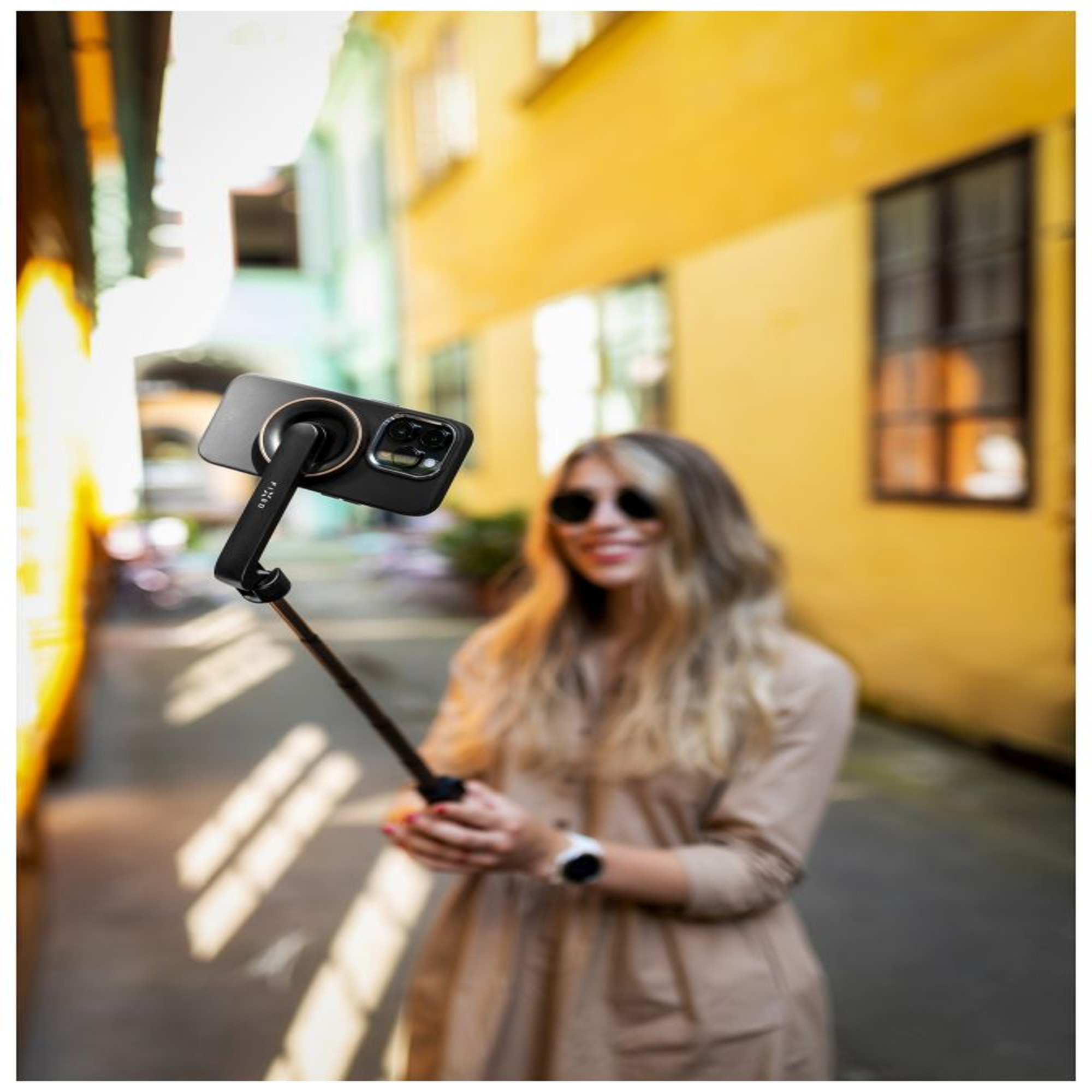 Frau macht ein Selfie mit einem Telefon und Selfie-Stick. Gelber und brauner Hintergrund.