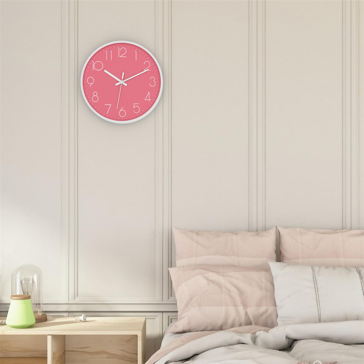 Rosa Uhr an einer Wand. Weiße Zahlen und Zeiger. Bett mit Kissen darunter.
