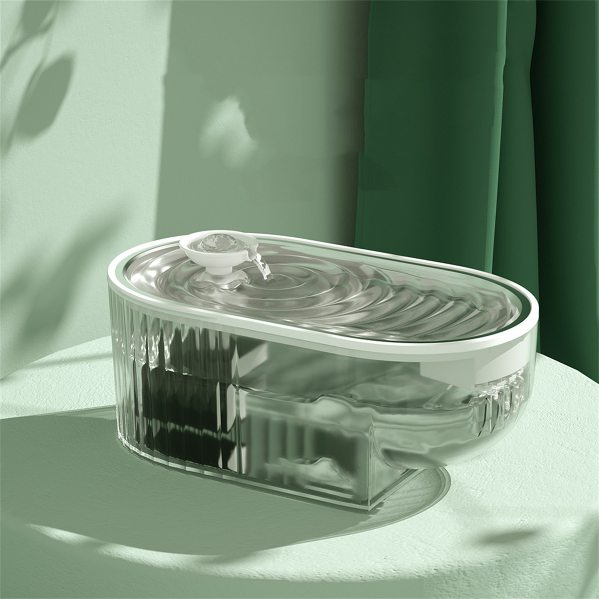 Transparenter Trinkbrunnen für Haustiere. Wasser fließt in das Becken. Grüne Vorhänge im Hintergrund.