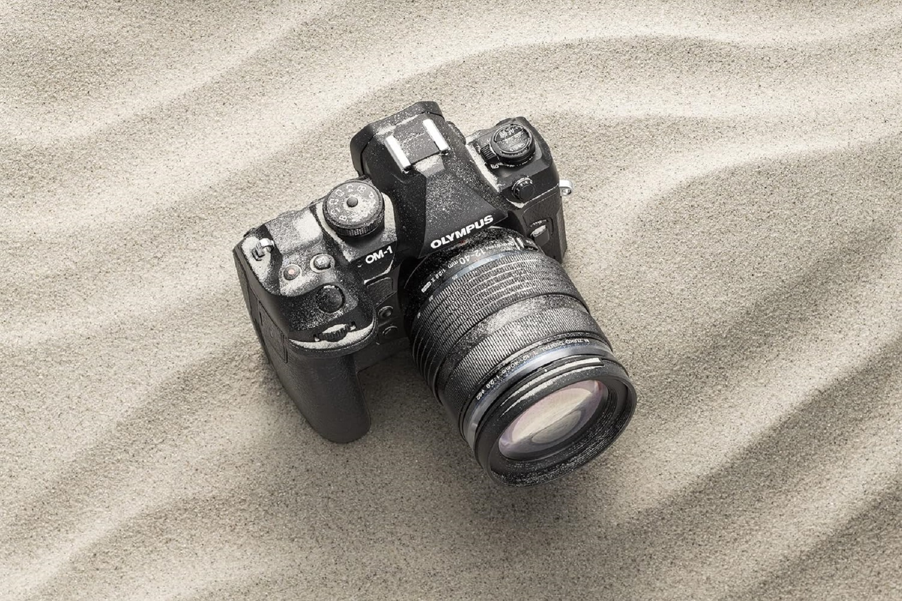 Olympus Kamera auf Sand. Kameragehäuse und Objektiv sind auf dem Sand sichtbar.