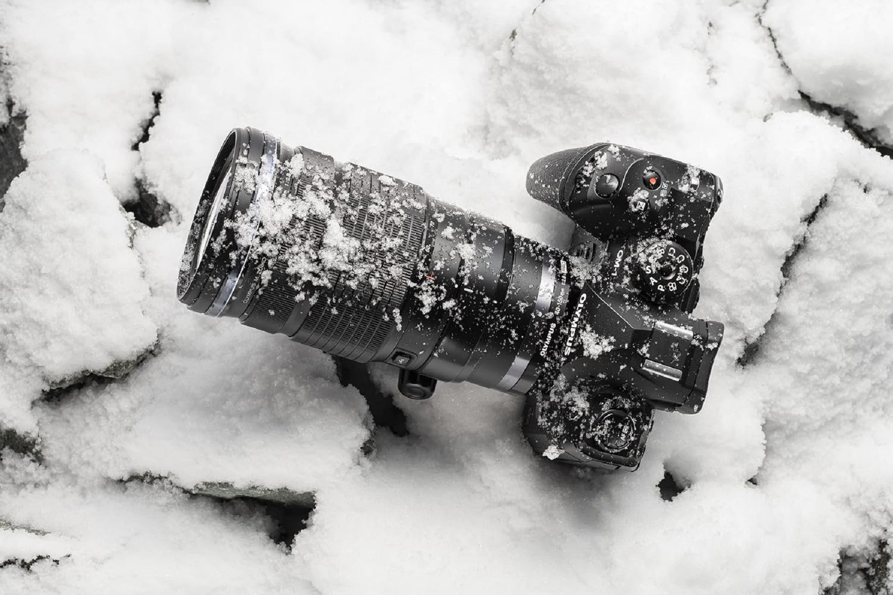 Schwarze Kamera mit schneebedecktem Objektiv, liegt auf einer schneebedeckten Oberfläche. Draufsicht, Studioaufnahme, Winterszene.