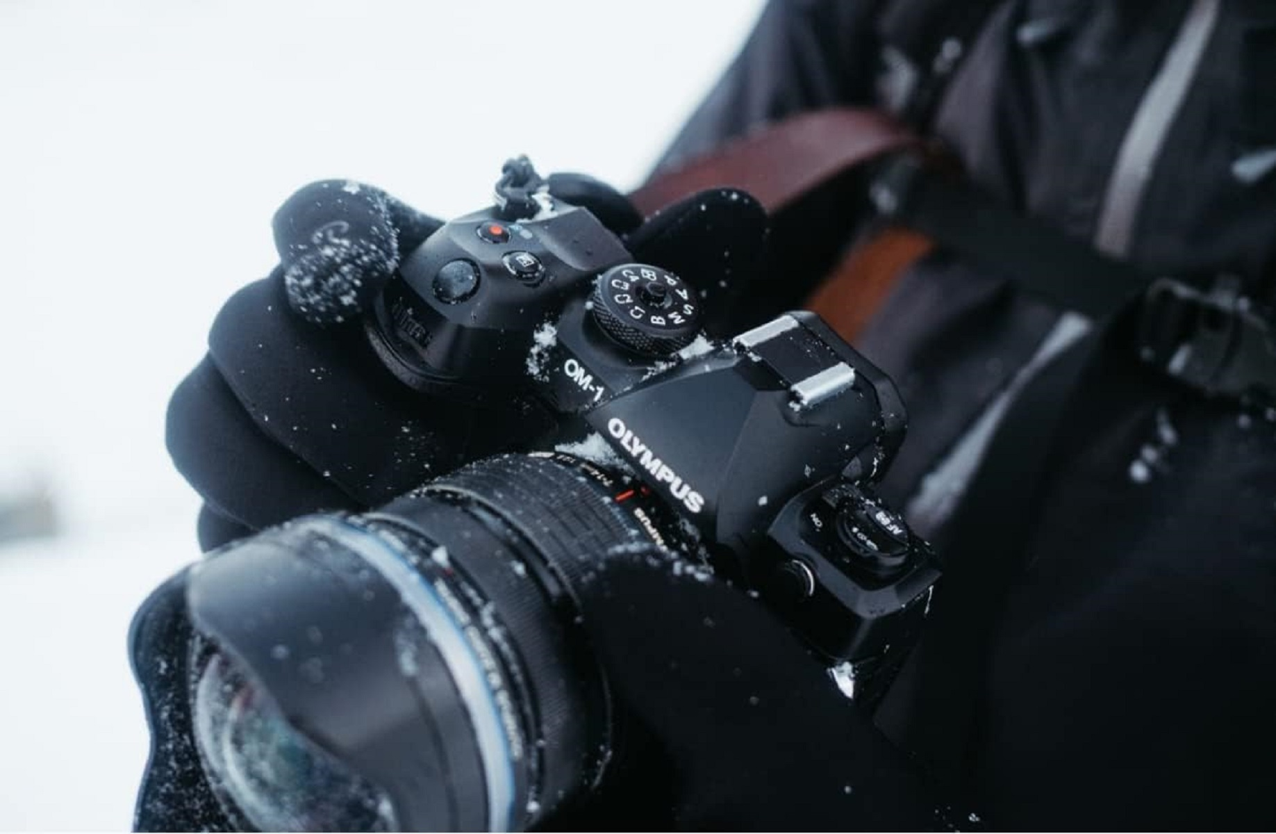 Schwarze Kamera in schwarzen Handschuhen. Die Marke Olympus ist sichtbar.