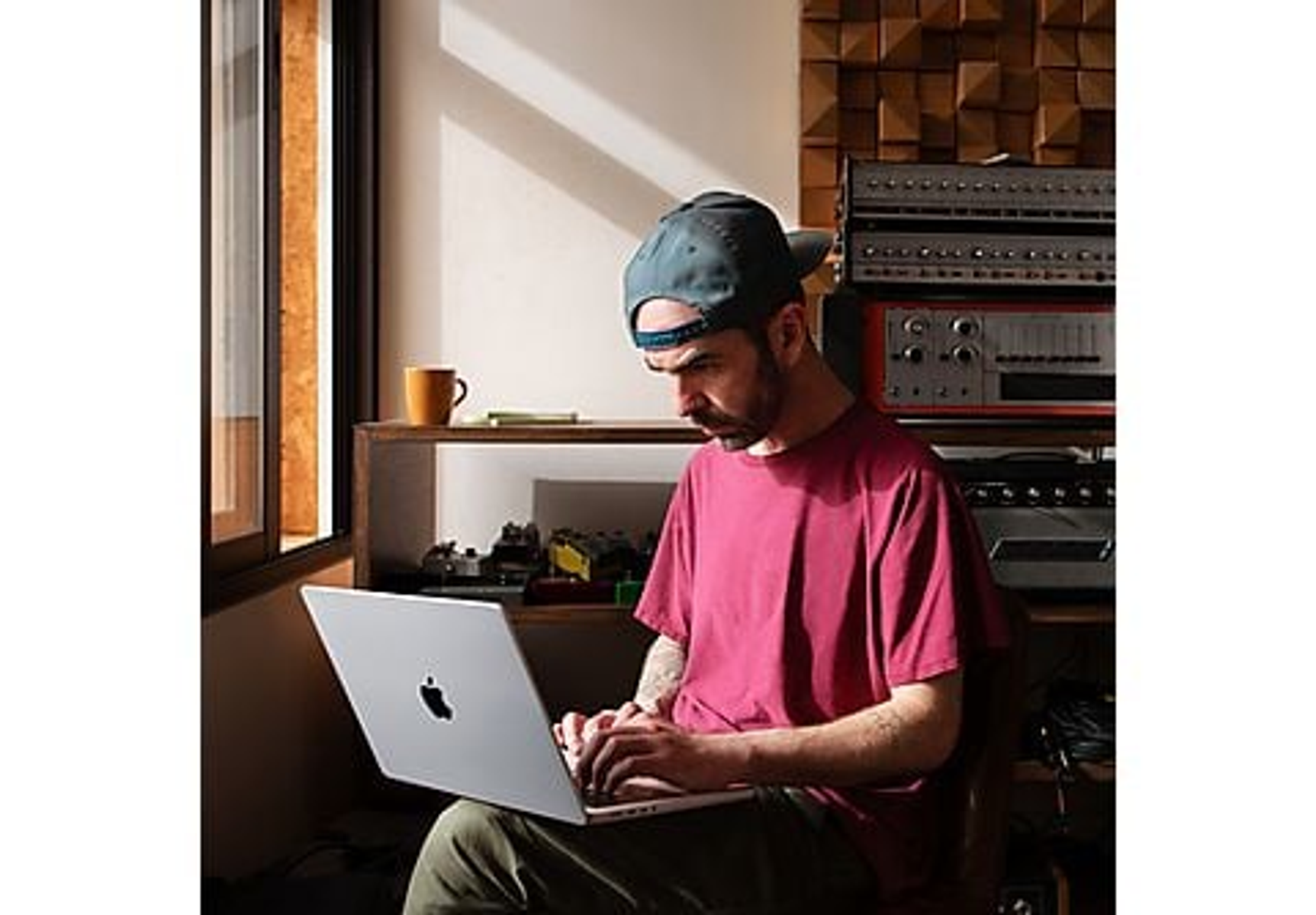 Man wearing a cap, working on a laptop. Studio with wooden panels and equipment.