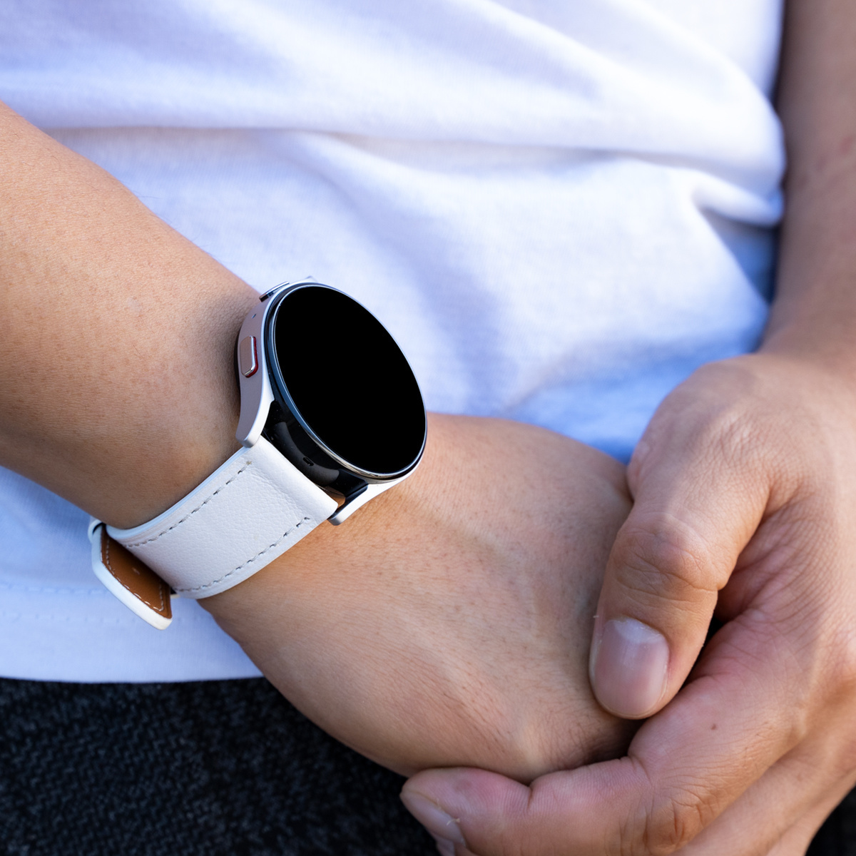 Eine Smartwatch am Handgelenk mit weißem Band und brauner Lederunterseite.