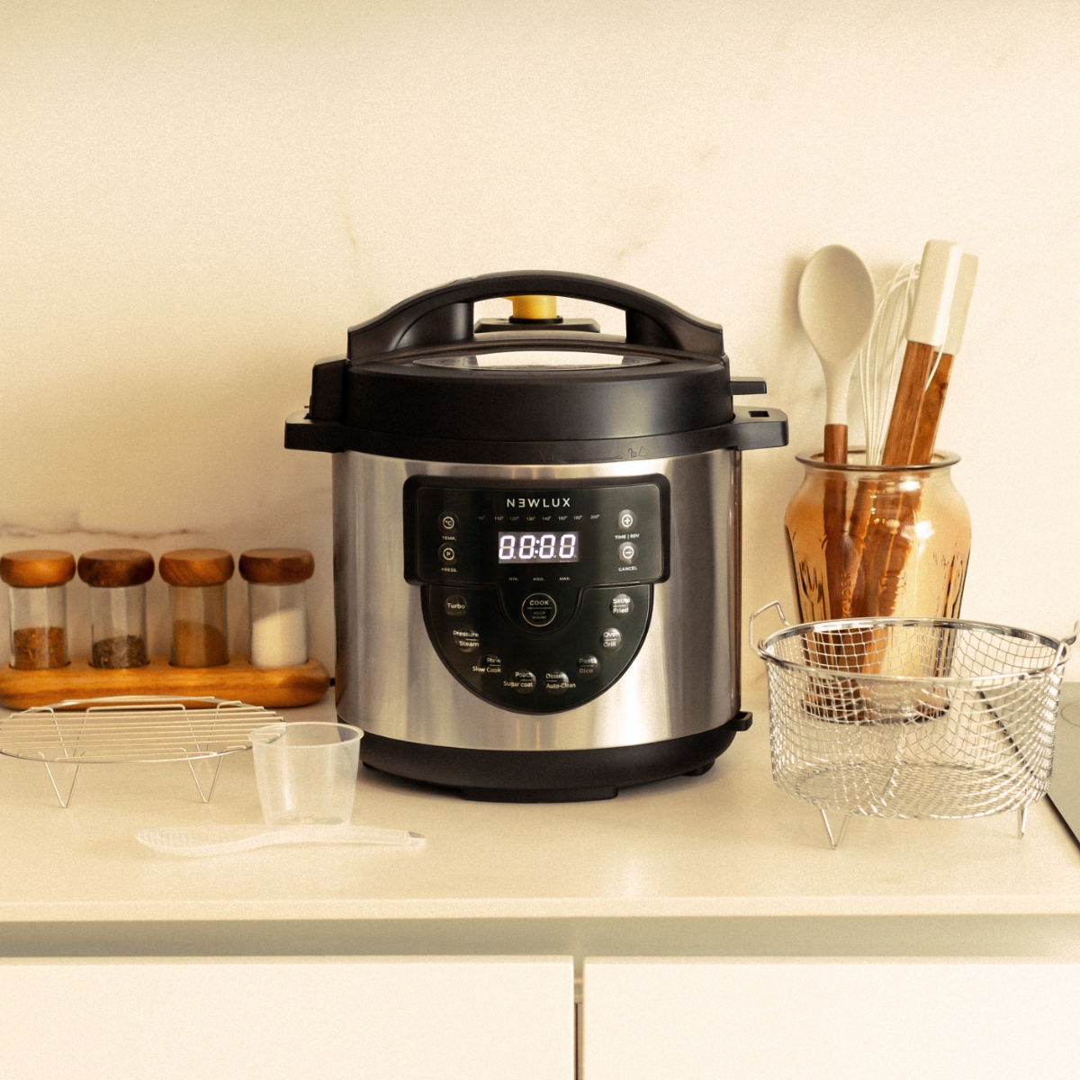 Olla a presión de acero inoxidable y accesorios en una encimera de cocina. Se ven especias y utensilios.