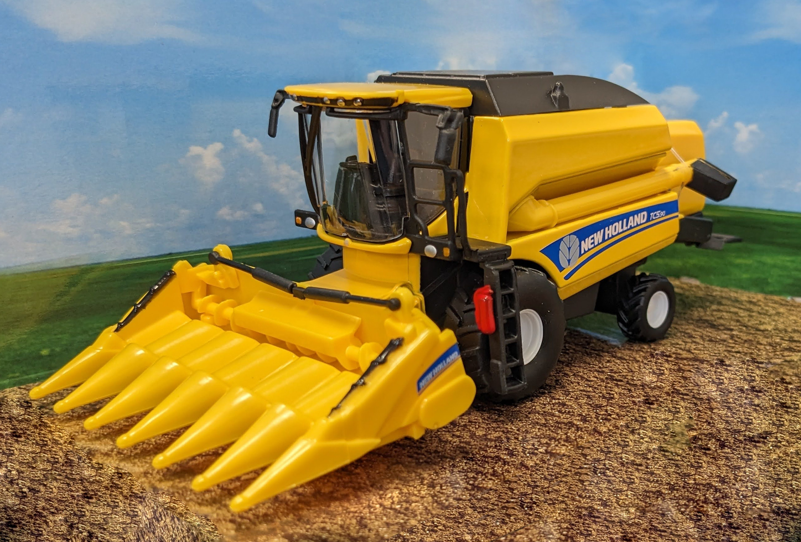 Gelbes New Holland Mähdreschermodell vor Feldhintergrund.