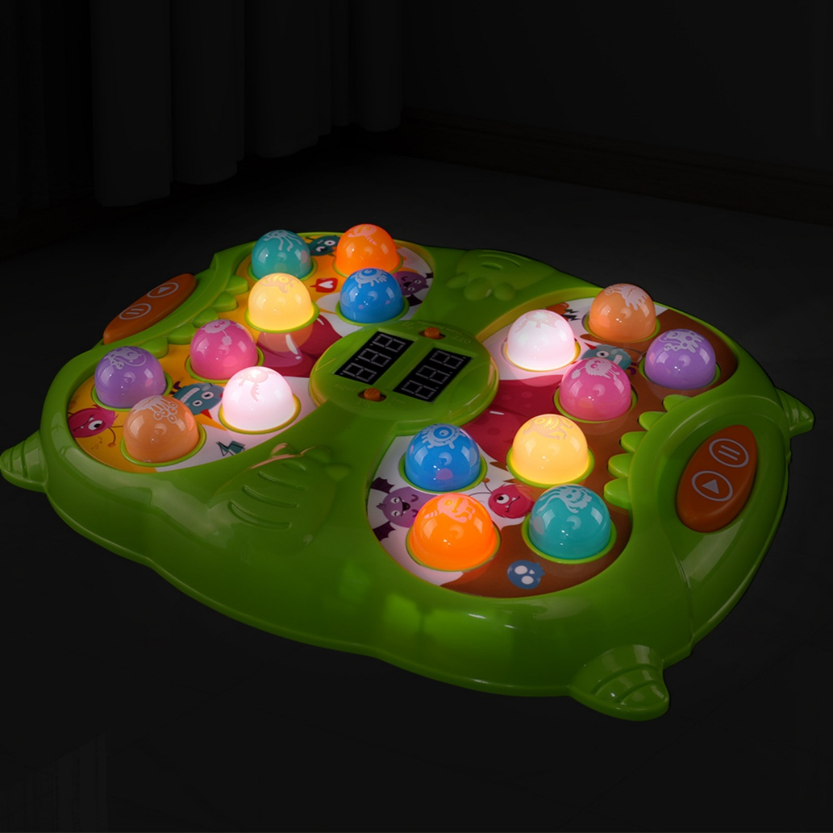 Grünes Spielzeug mit bunten Lichtern und Knöpfen; dunkler Hintergrund.