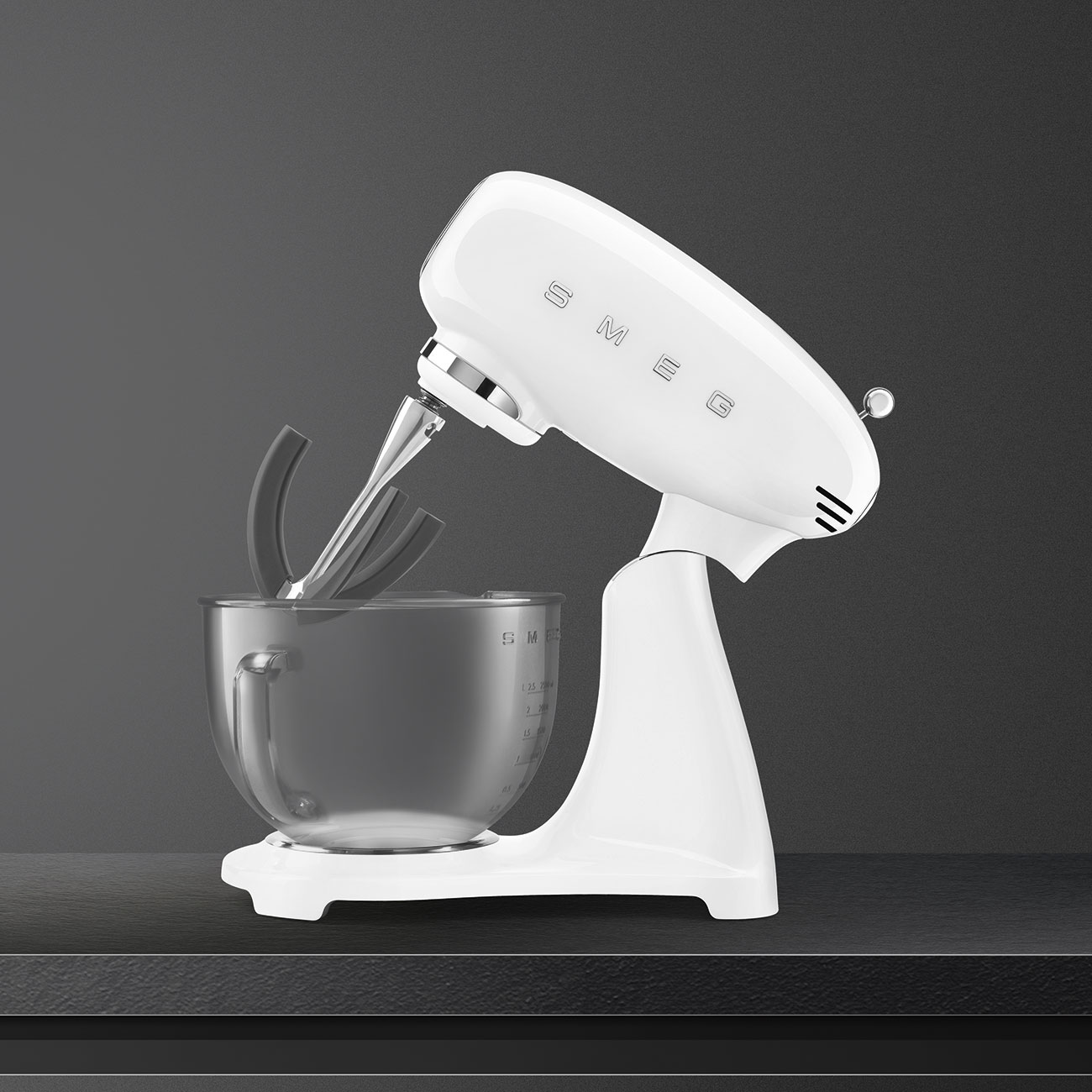 Weißer Küchenmixer mit Rührschüssel, auf dunkler Oberfläche. Grauer Hintergrund.