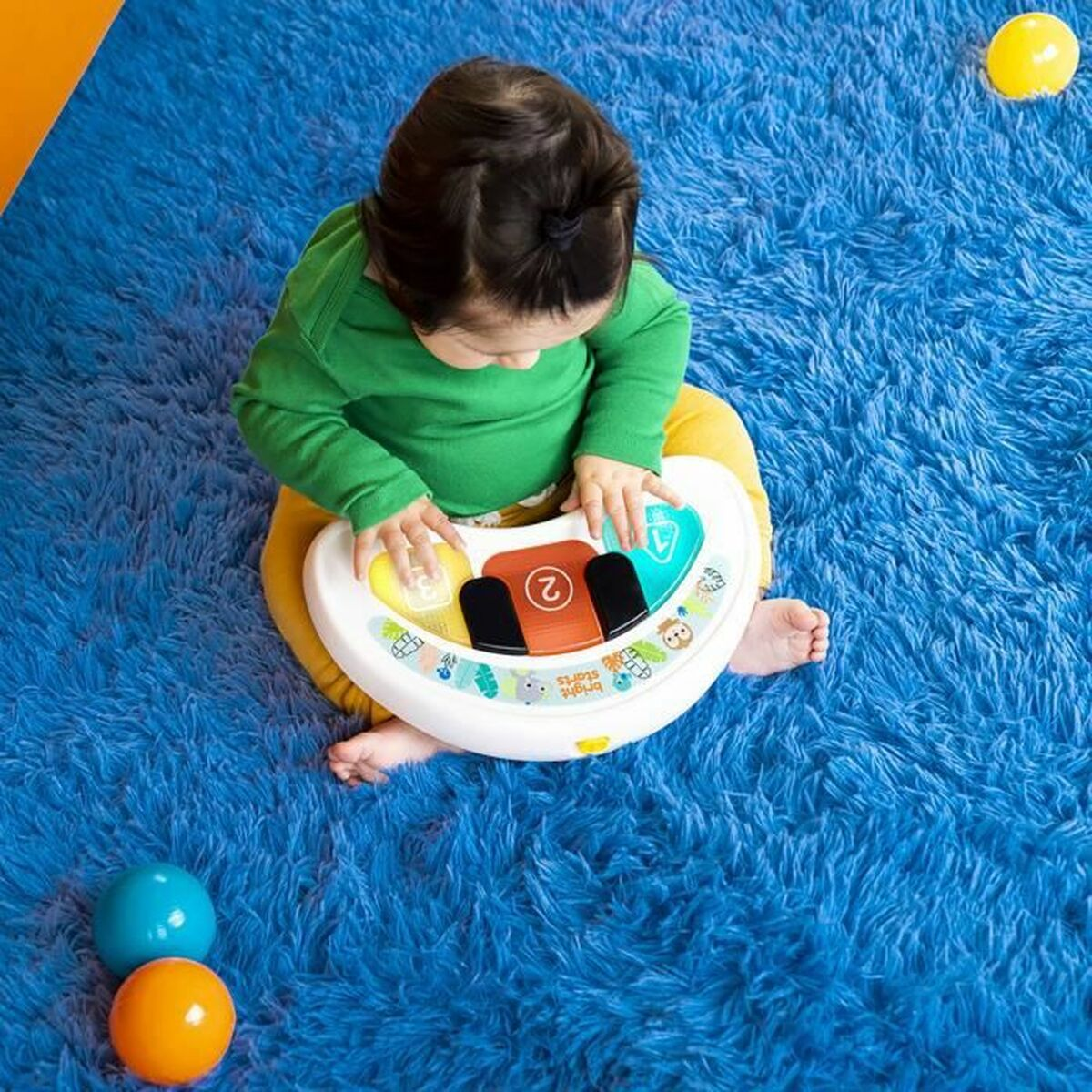 Baby spielt mit Spielzeug auf blauem Teppich, gelbe und blaue Bälle, Draufsicht.