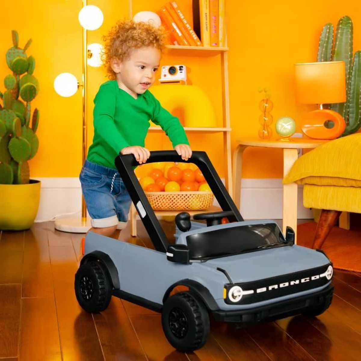 Ein Kleinkind steuert ein graues Spielzeugauto in einem hellorangenen Raum. Das Auto hat einen schwarzen Griff.