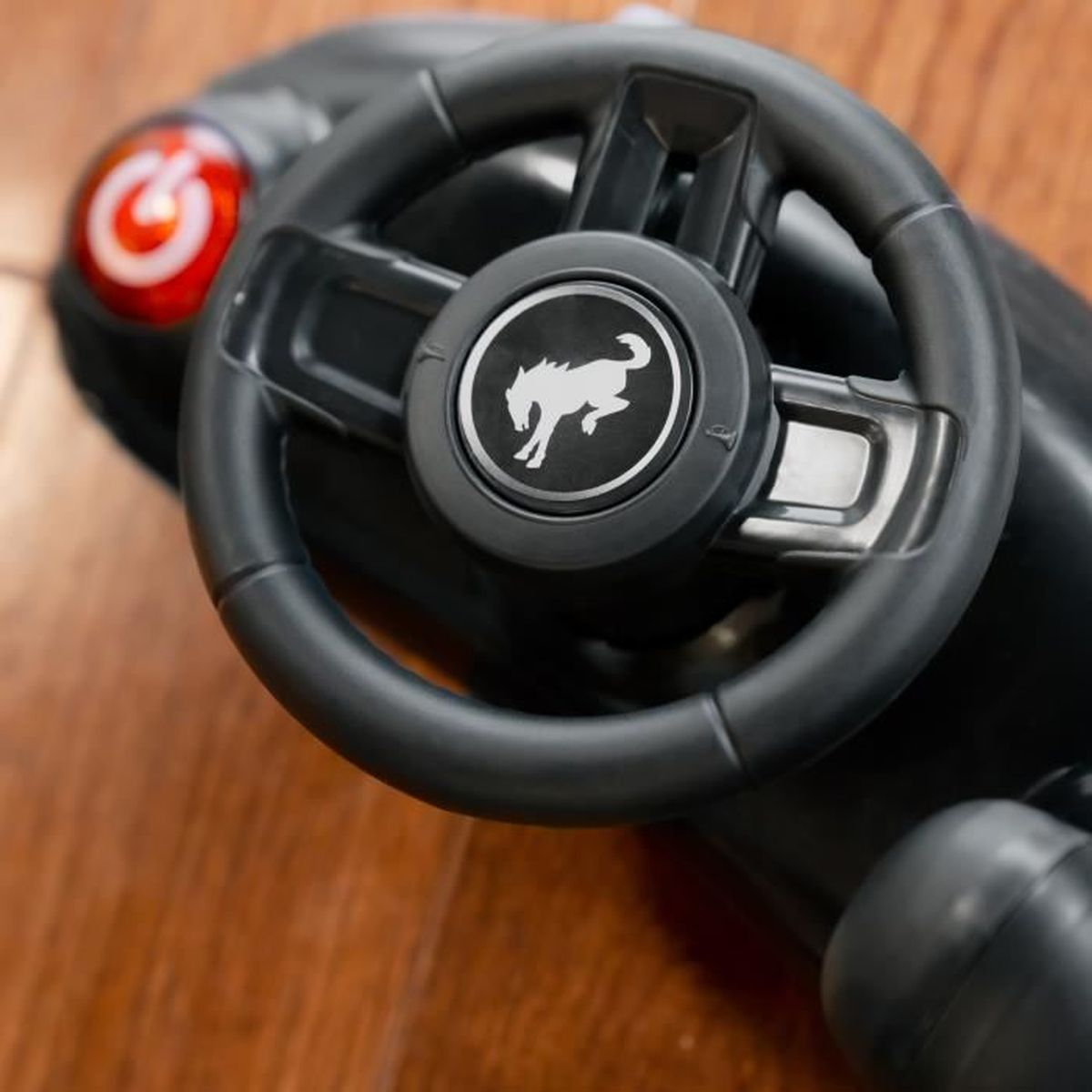 Schwarzes Lenkrad mit Logo eines Pferdes. Das Rad ist Teil eines Spielzeugautos, auf einer Holzoberfläche.