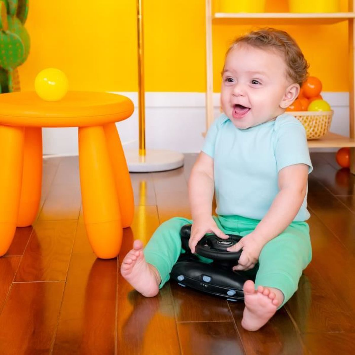 Glückliches Baby sitzt mit schwarzem Spielzeug, lächelt, in buntem Raum.