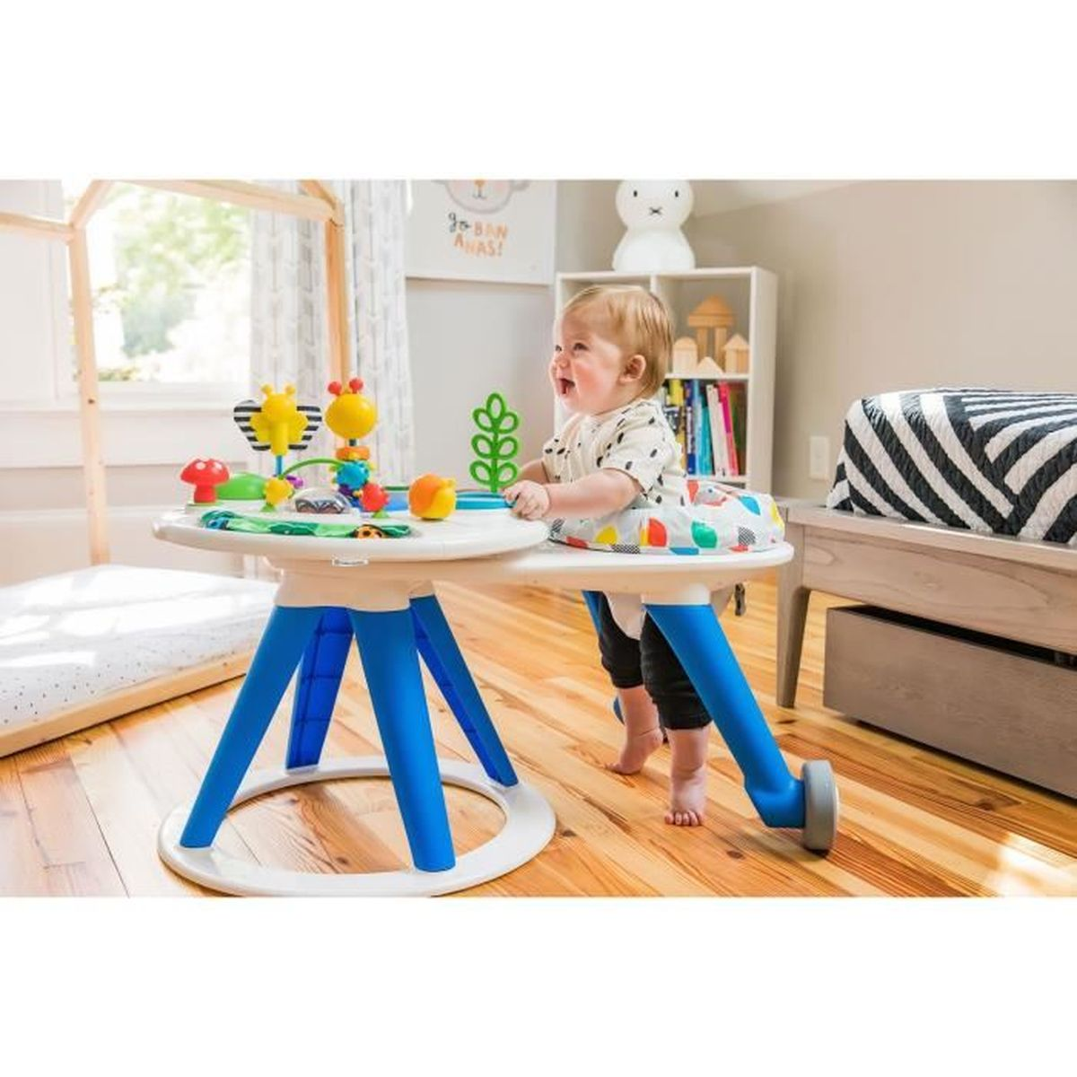 Baby im Lauflerner spielt mit Spielzeug auf einem weiß-blauen Tisch, helle Raumeinstellung.
