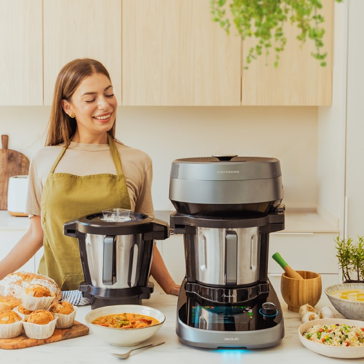 Una donna sorride in una cucina con robot da cucina e cibo. Altre persone sullo sfondo.