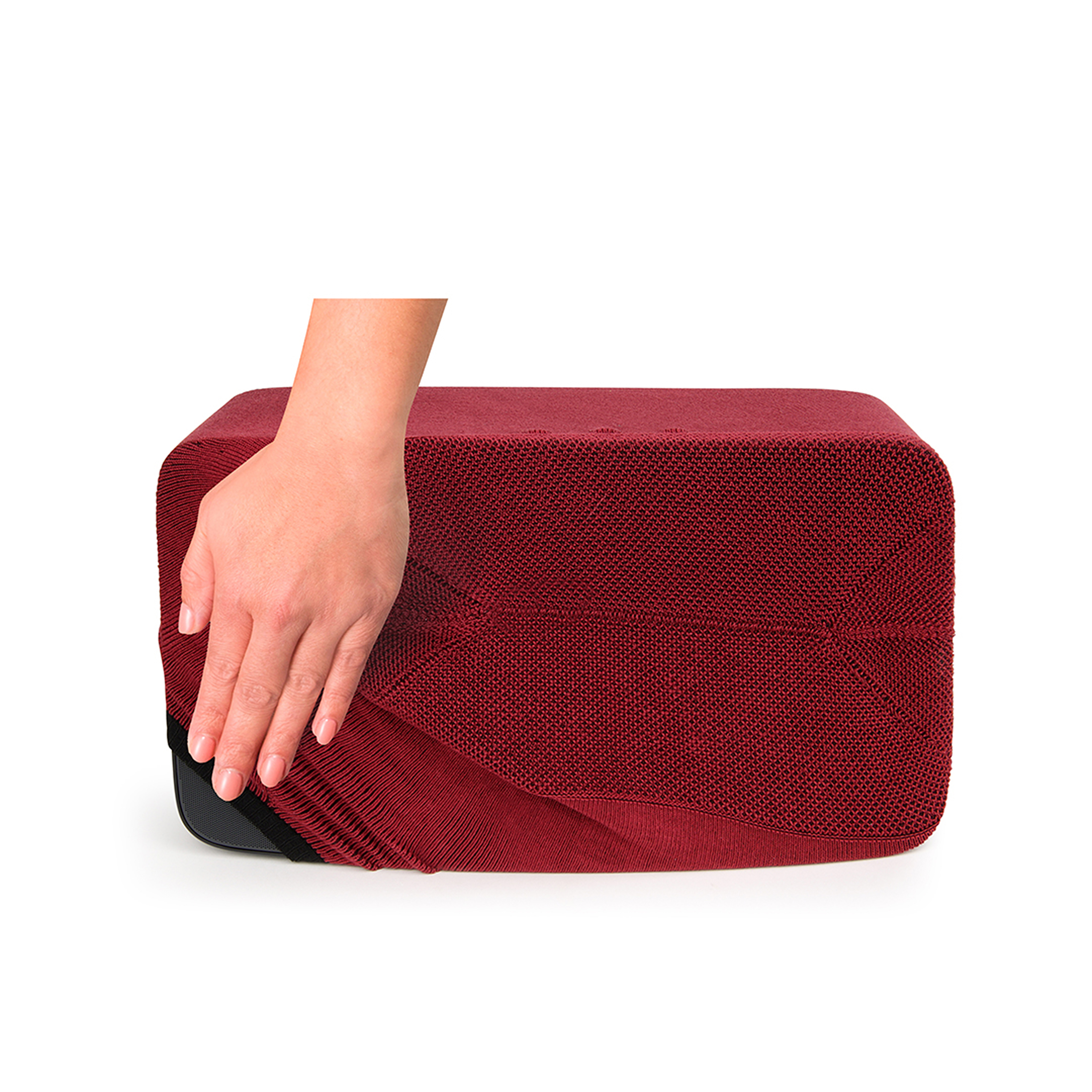 Une main touche un objet rouge texturé. L'objet est rectangulaire et repose sur du blanc.