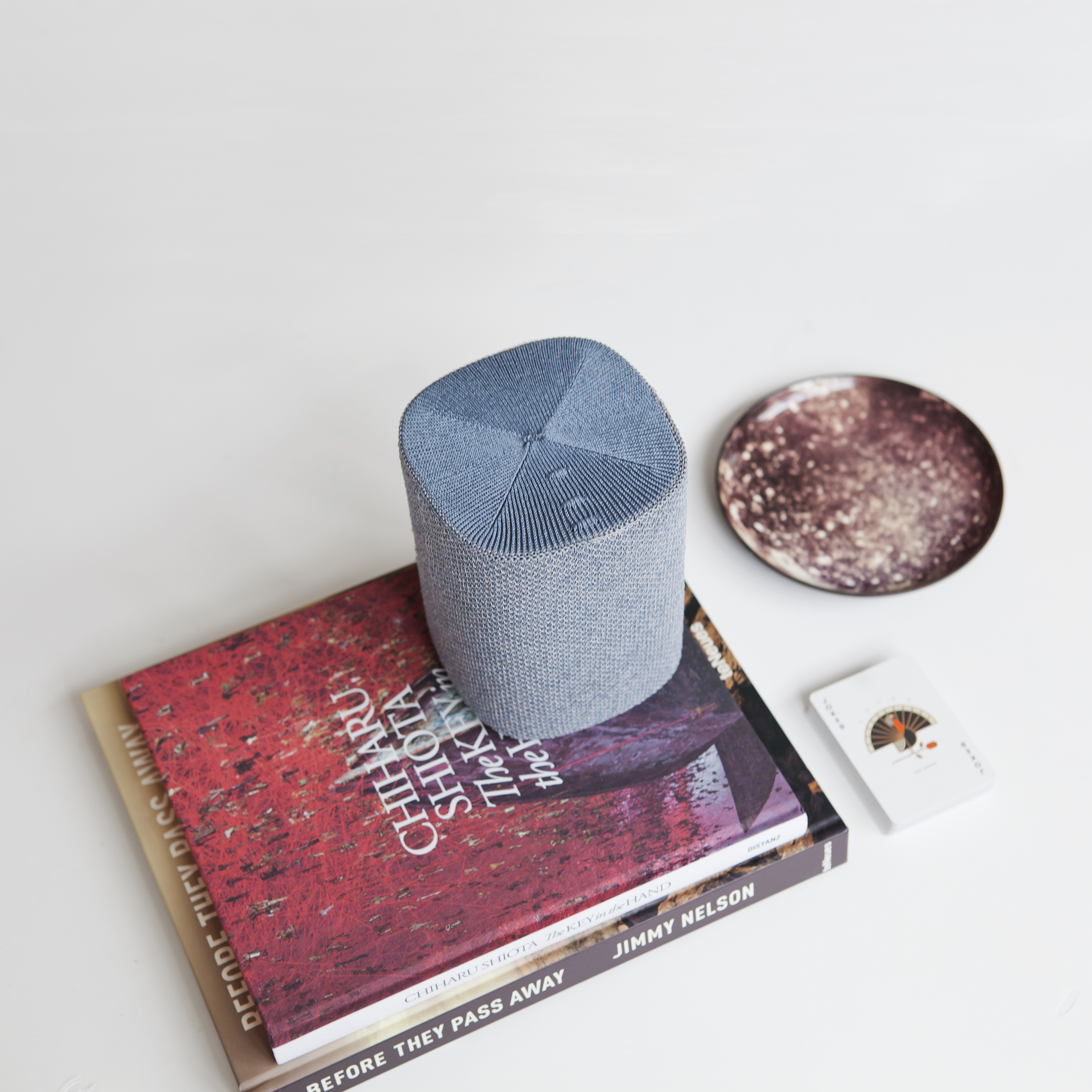 Livres, une petite assiette et une carte sur une surface blanche. Un objet en mesh bleu sur des livres.