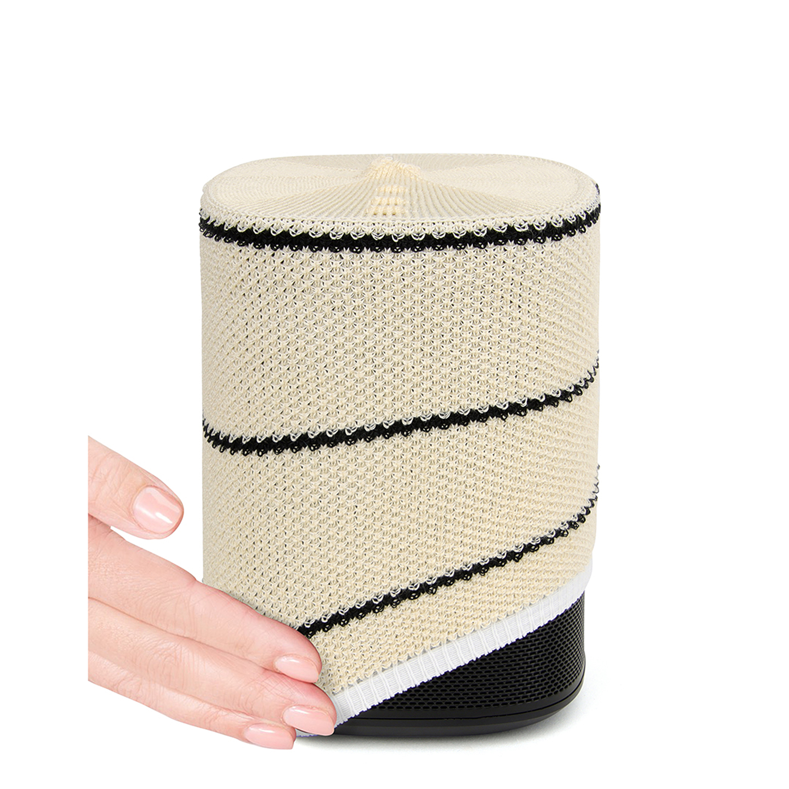 Une main touche un haut-parleur cylindrique crème avec une base et des détails noirs.