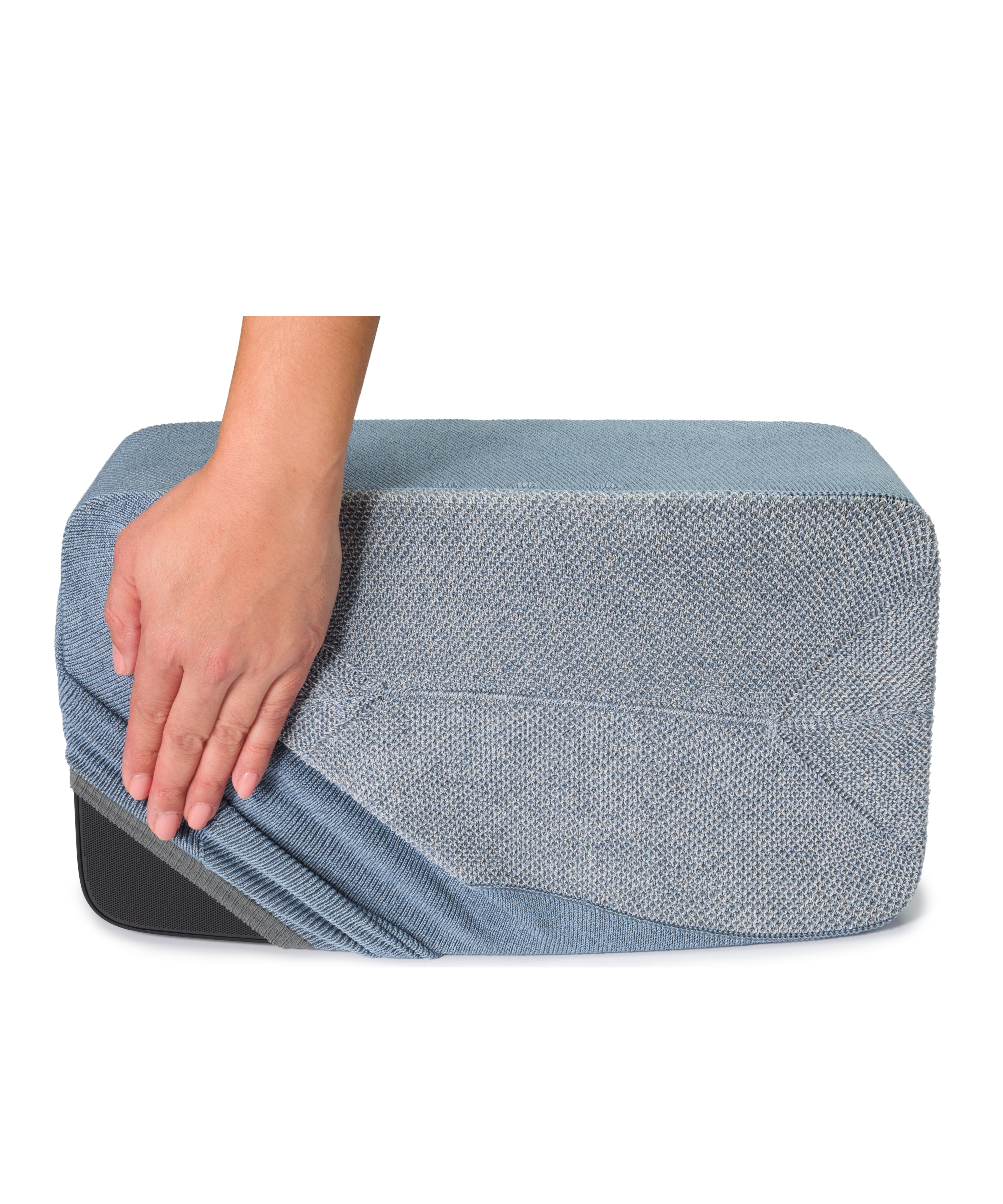 Une main tire une housse bleu clair sur un pouf rectangulaire gris.