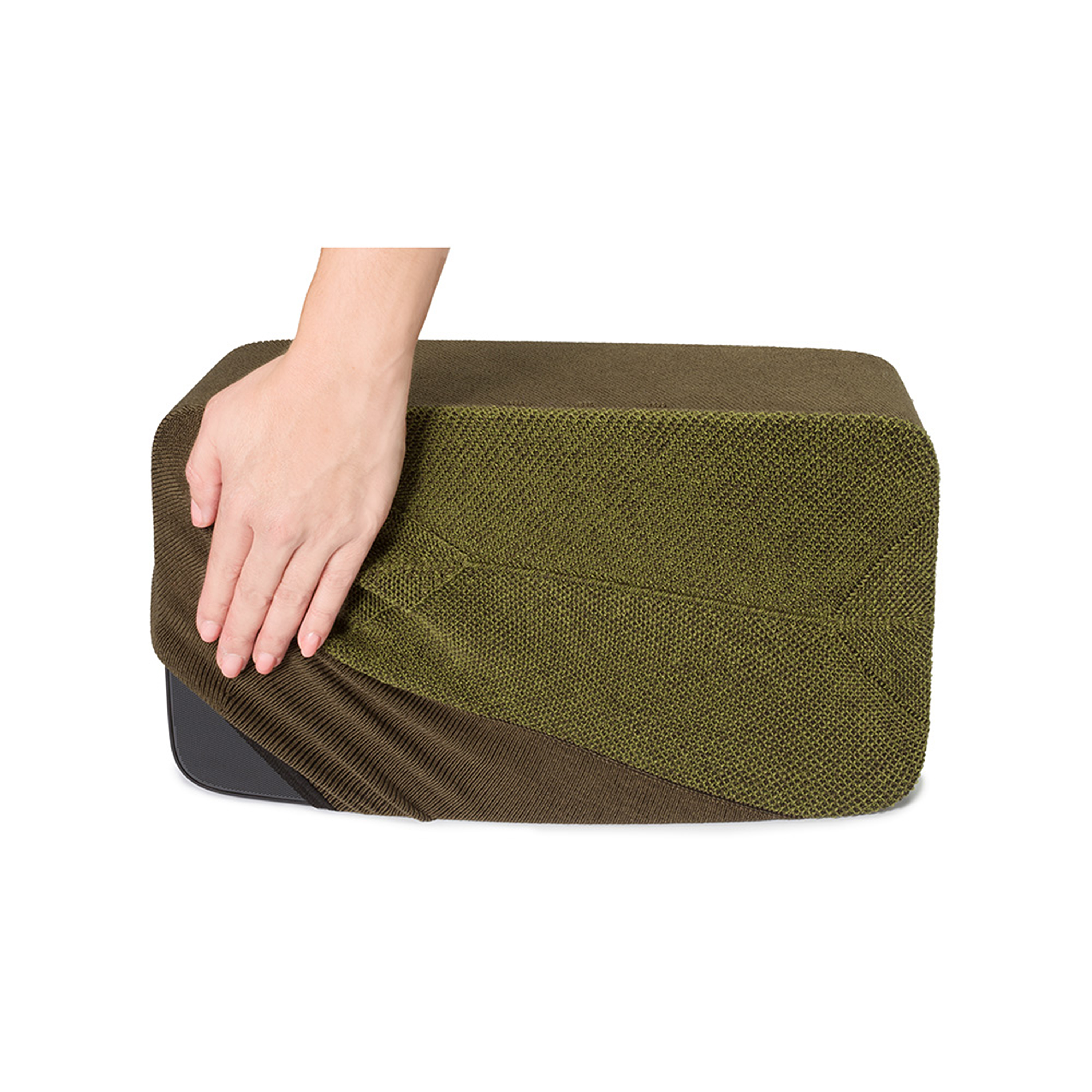 Une main tire un tissu texturé vert olive sur un objet sombre, sur un fond blanc.