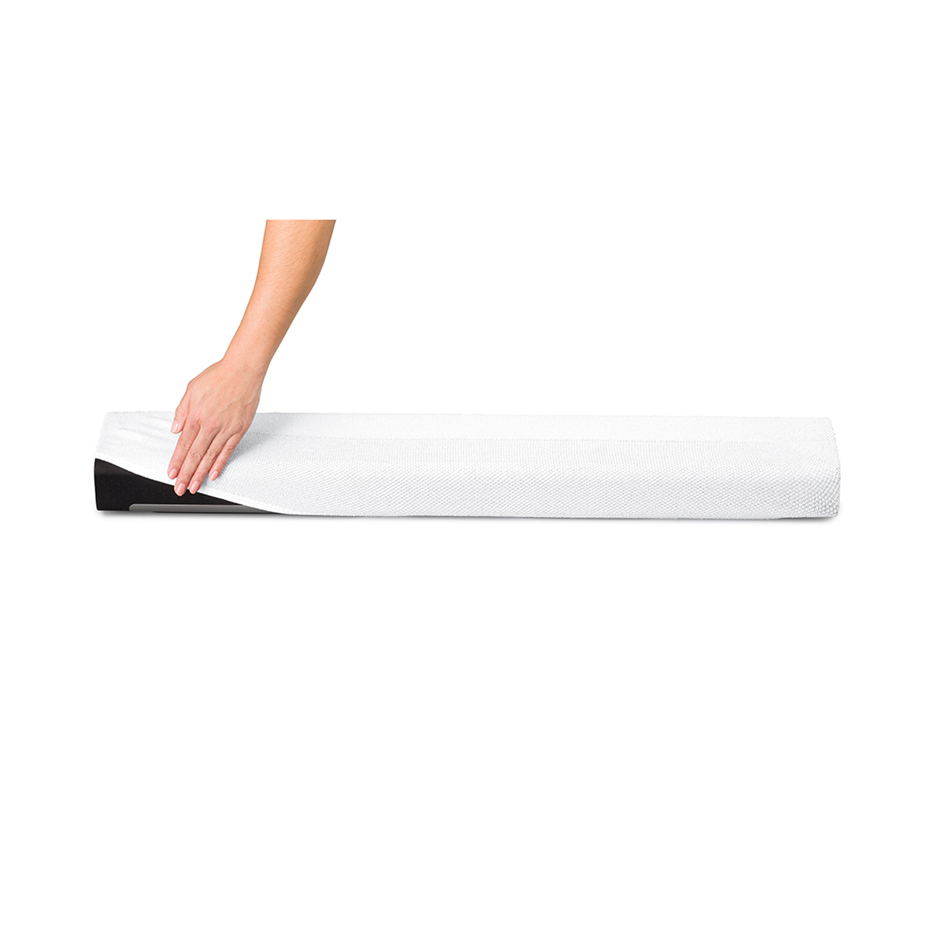 Une main lisse un drap blanc sur un long matelas en mousse blanc roulé, sur fond blanc.