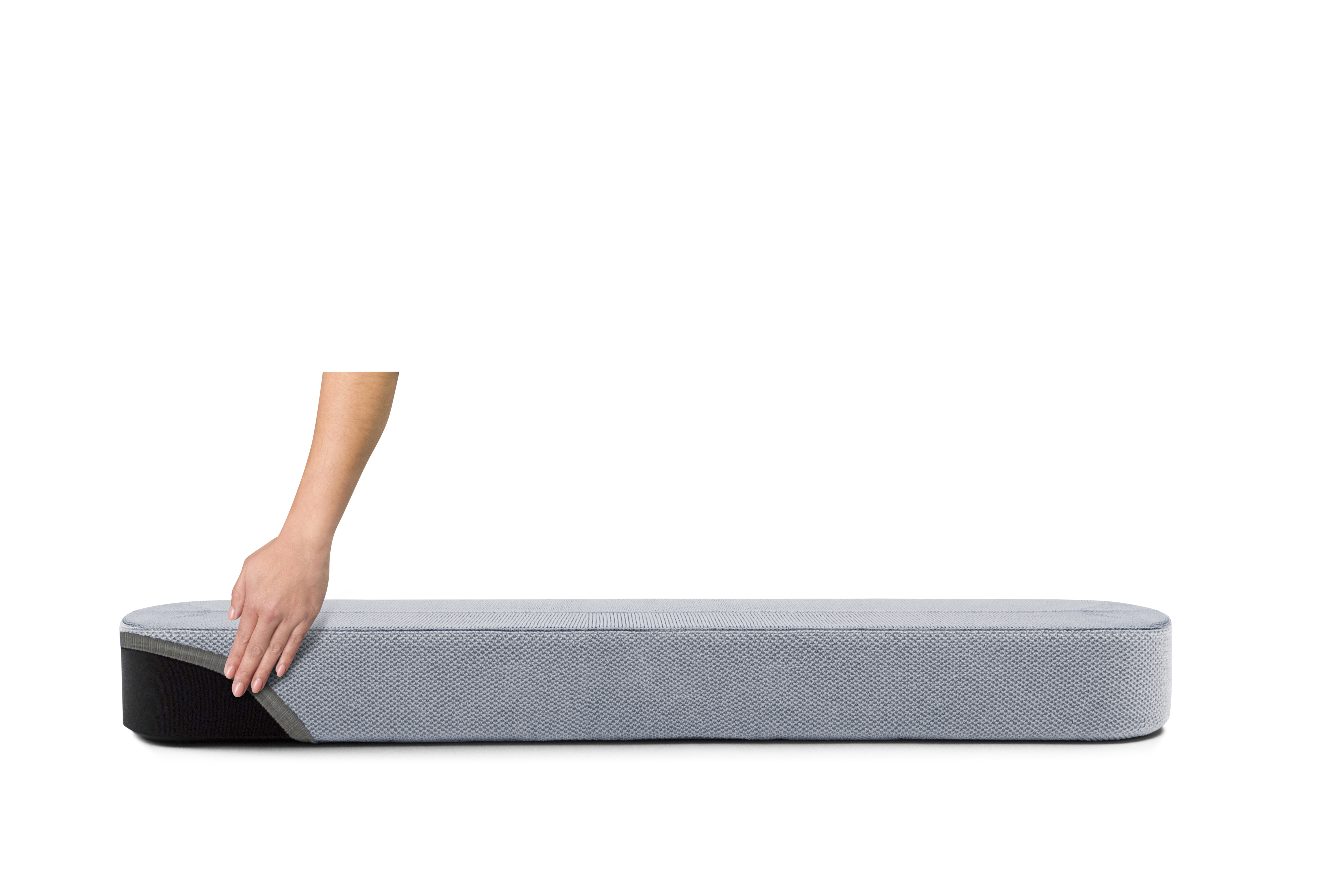 Une main touche un matelas gris avec un détail noir à l'extrémité.