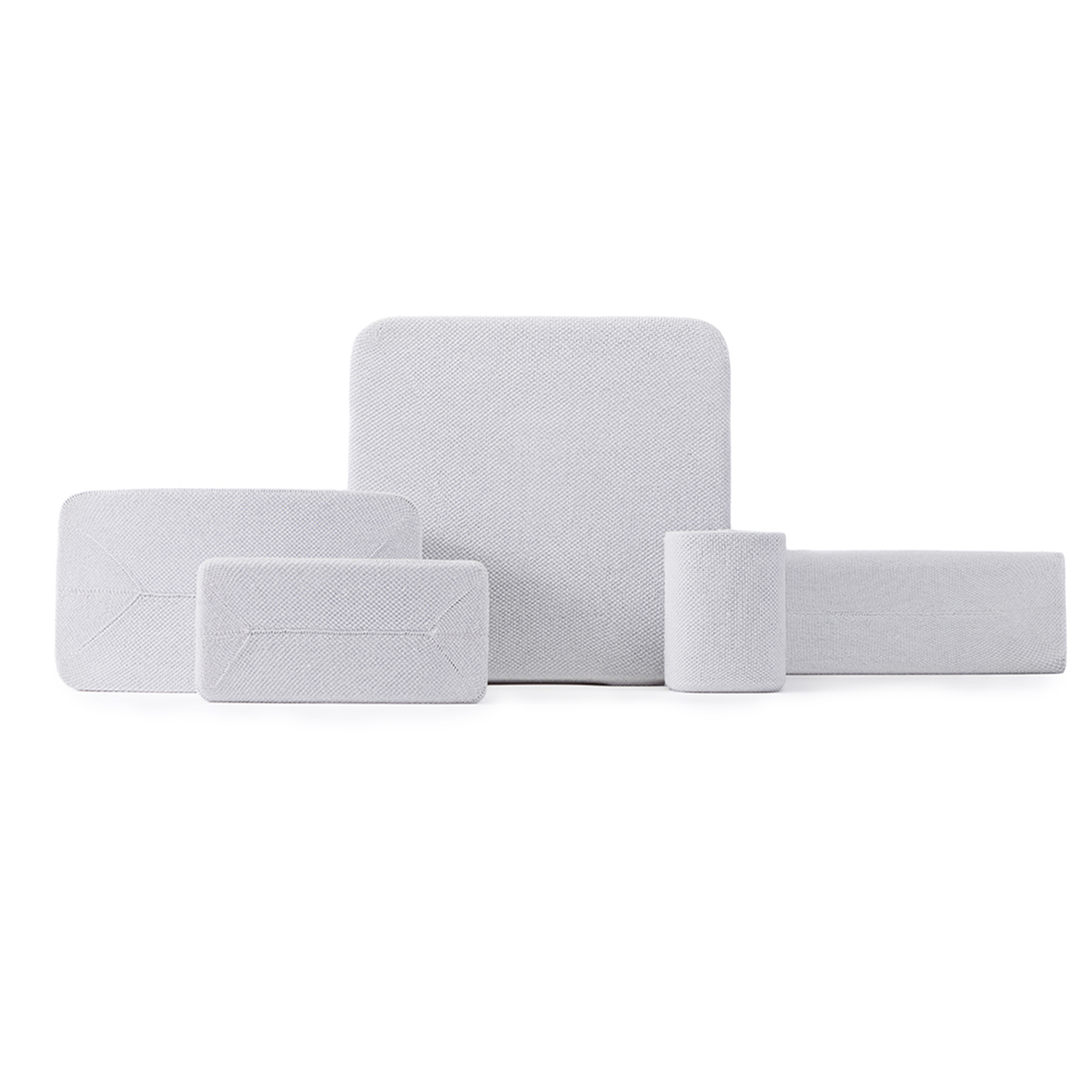 Divers coussins blancs texturés et objets rectangulaires disposés sur une surface blanche.