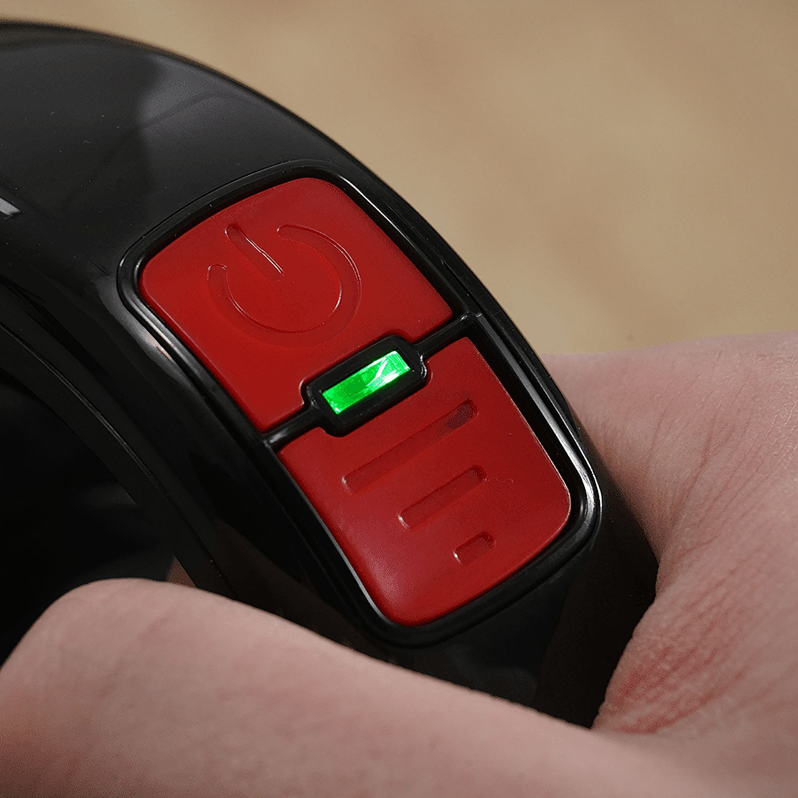 Un primo piano di un pulsante di accensione rosso con una luce verde. Le dita di una persona sono visibili.