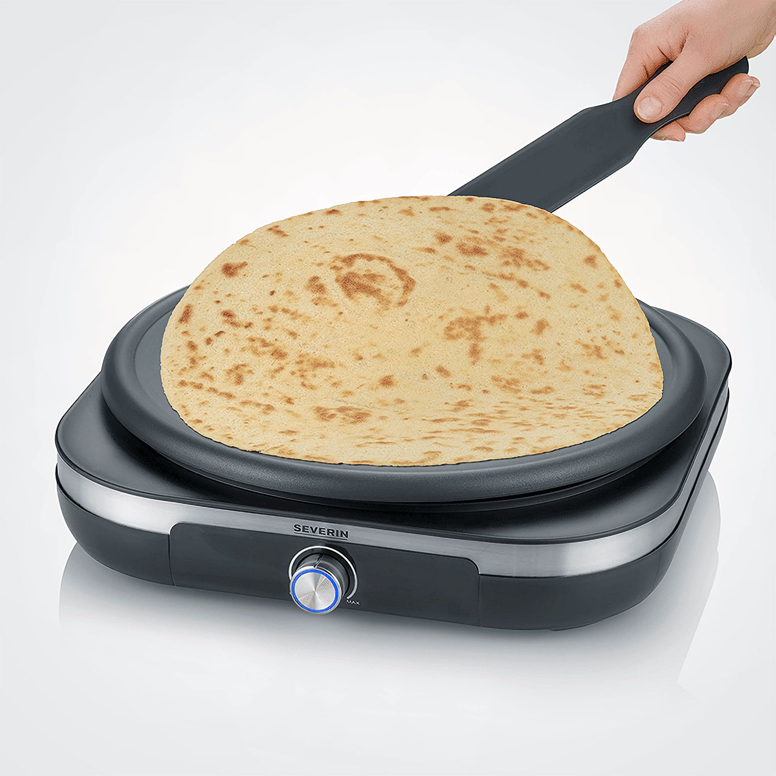 Tortilla na czarnej elektrycznej płycie grillowej. Ręka używa szpatułki. Widoczne logo SEVERIN.