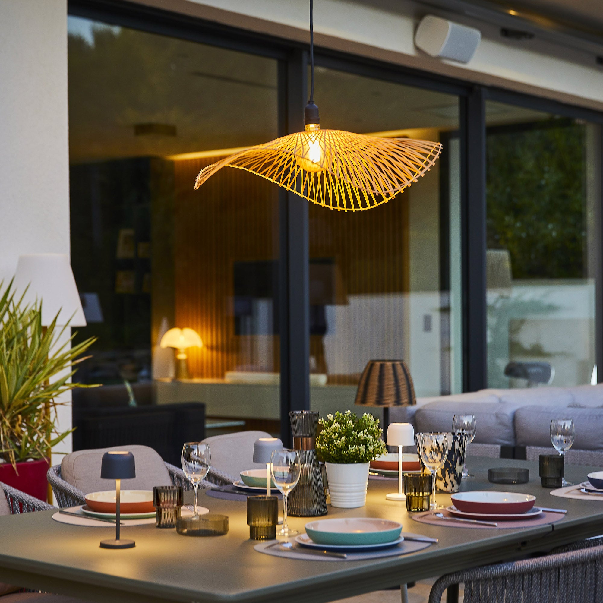 Esstisch im Freien mit Lampen, Gläsern und Essen, mit einer beleuchteten Lampe darüber.