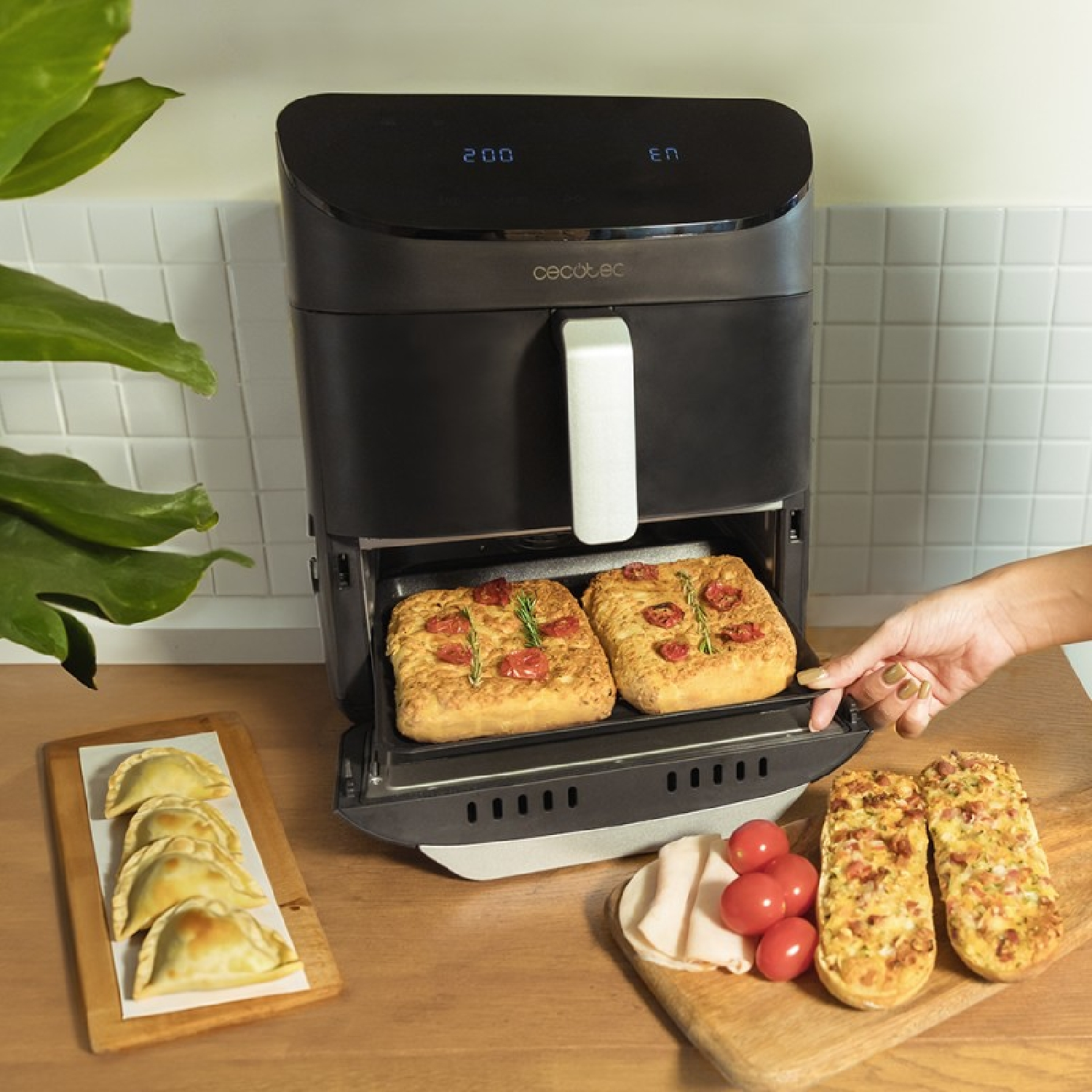 Czarna frytkownica powietrzna z jedzeniem w środku, z różnymi potrawami obok. Drewniana powierzchnia.