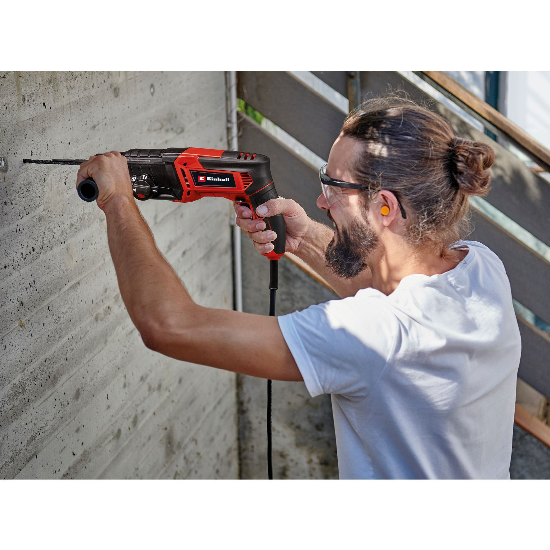 Mężczyzna wiercący w betonowej ścianie czerwoną wiertarką.