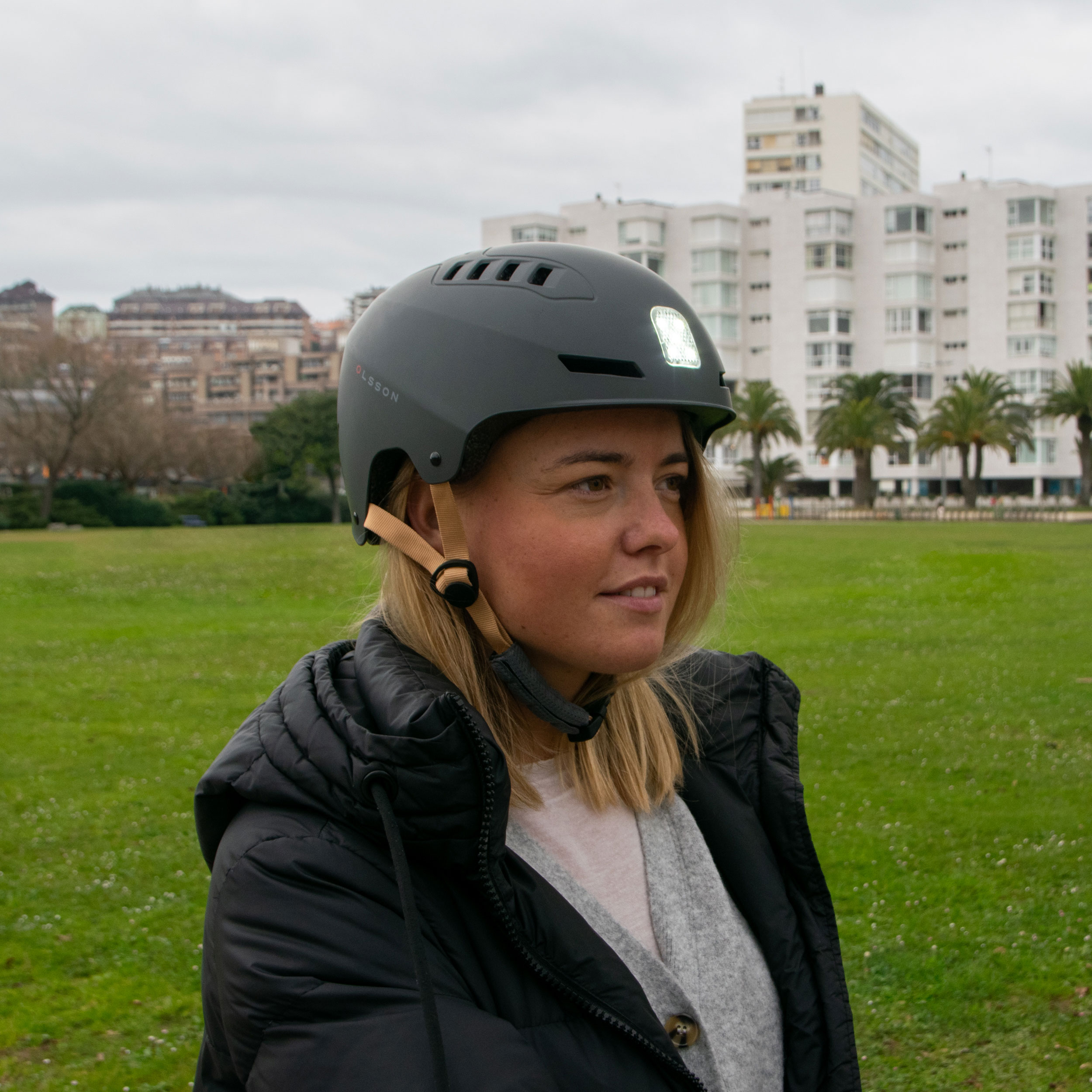 Mujer con casco gris con luz, de pie en un parque con césped verde.
