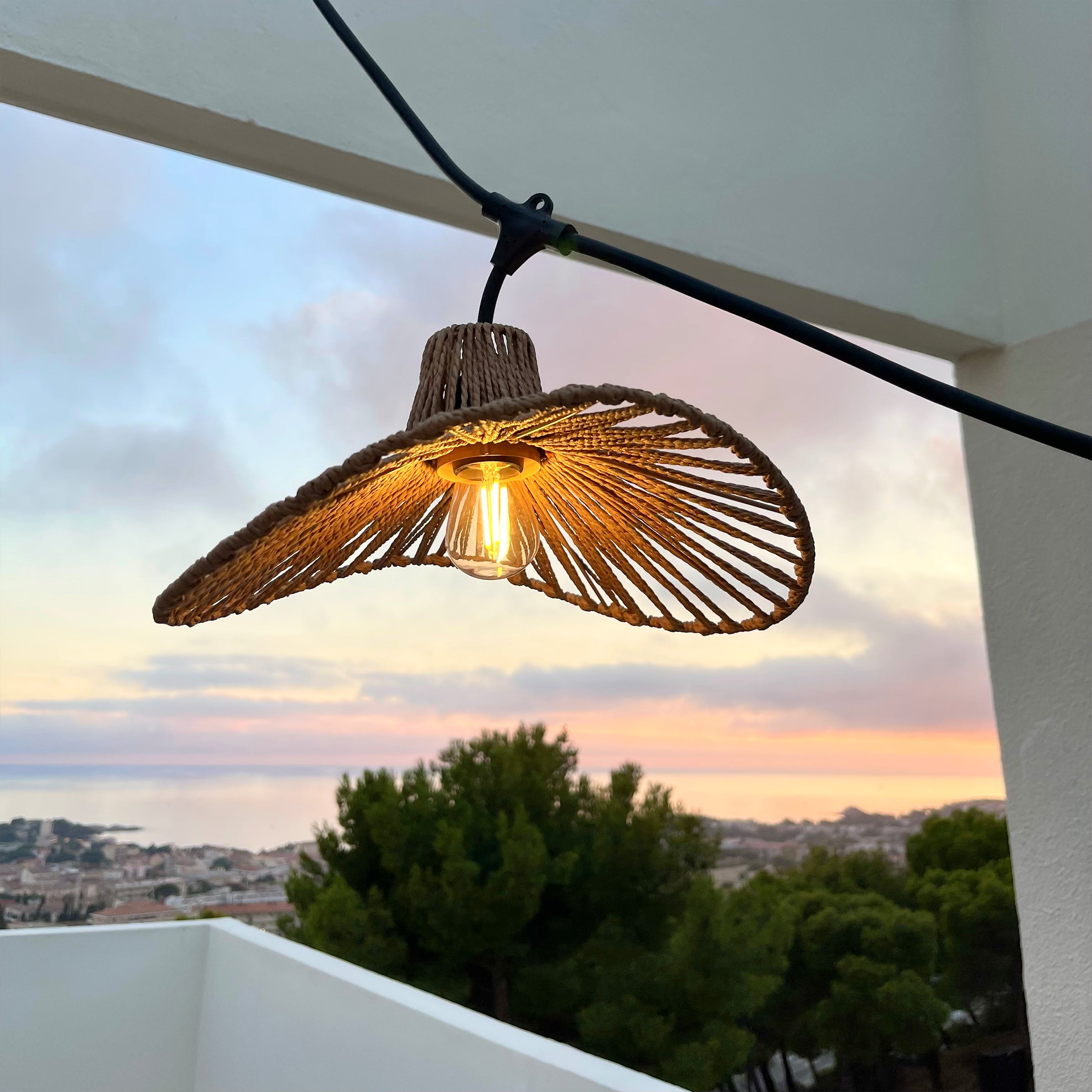 Eine Strohhutlampe mit leuchtender Glühbirne, die an einem Draht hängt, mit wunderschönem Sonnenuntergang.