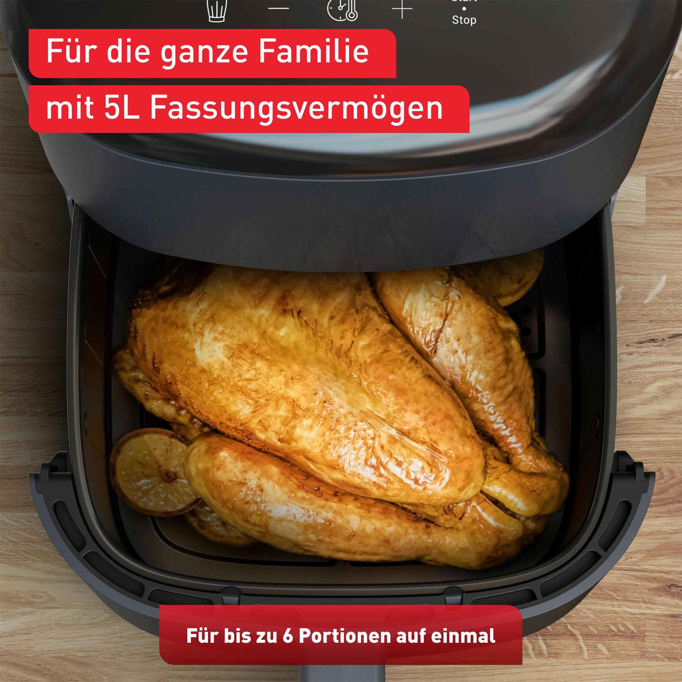 Frytkownica powietrzna z upieczonym kurczakiem w środku na drewnianej powierzchni.