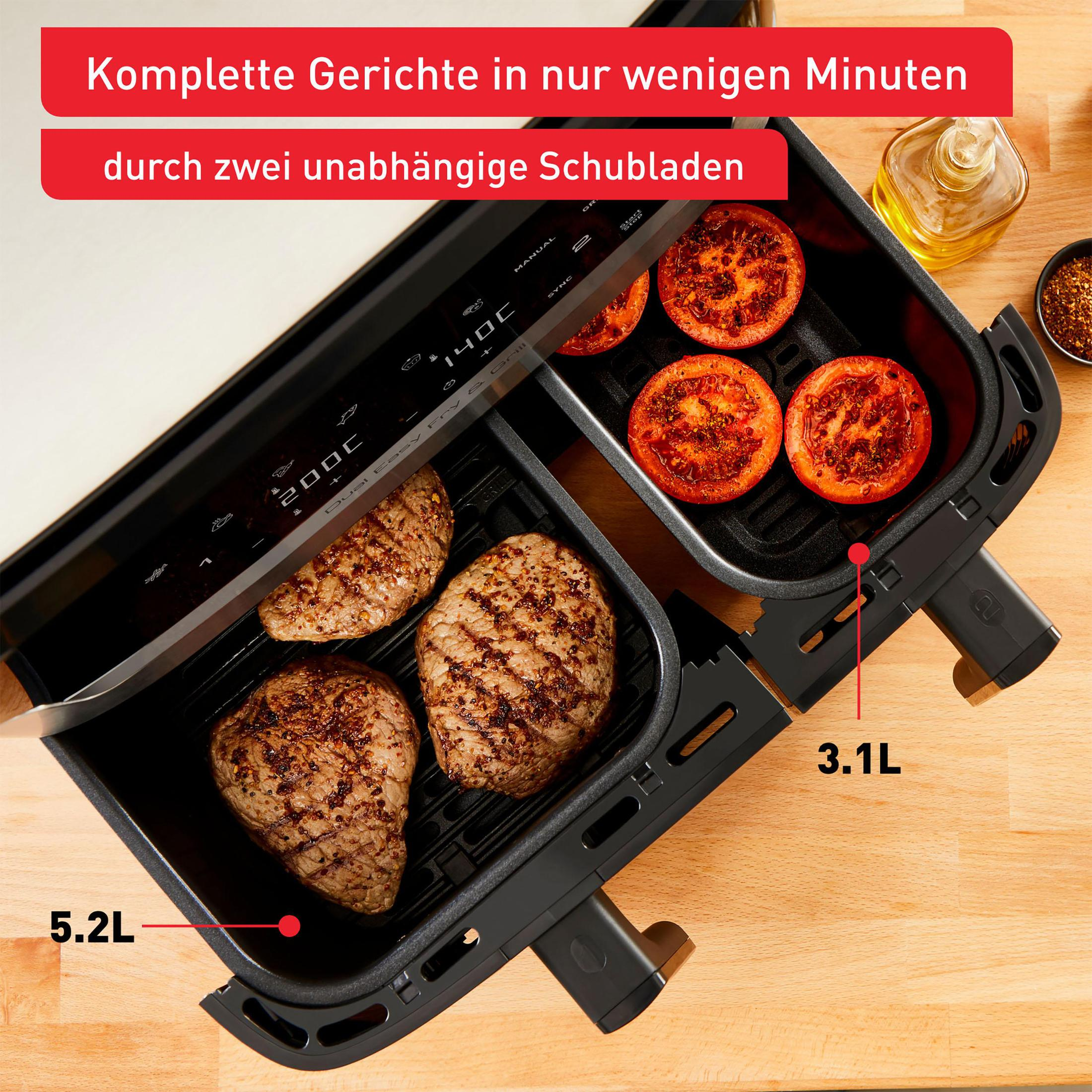 Eine Heißluftfritteuse mit zwei Fächern, mit Essen darin. Eins hat Steaks, das andere Tomaten.