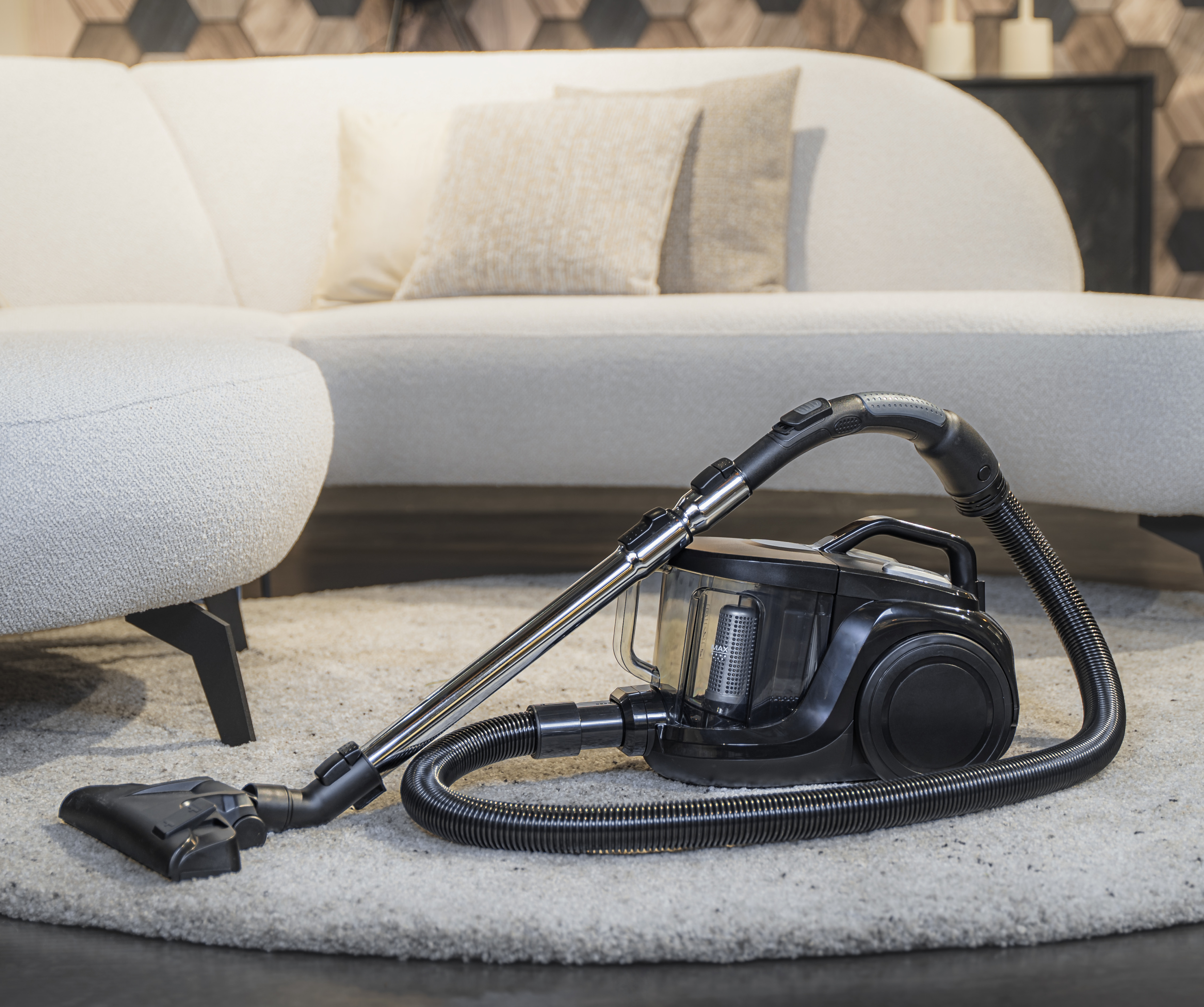 Black vacuum cleaner on a light rug. White sofa in the background.
