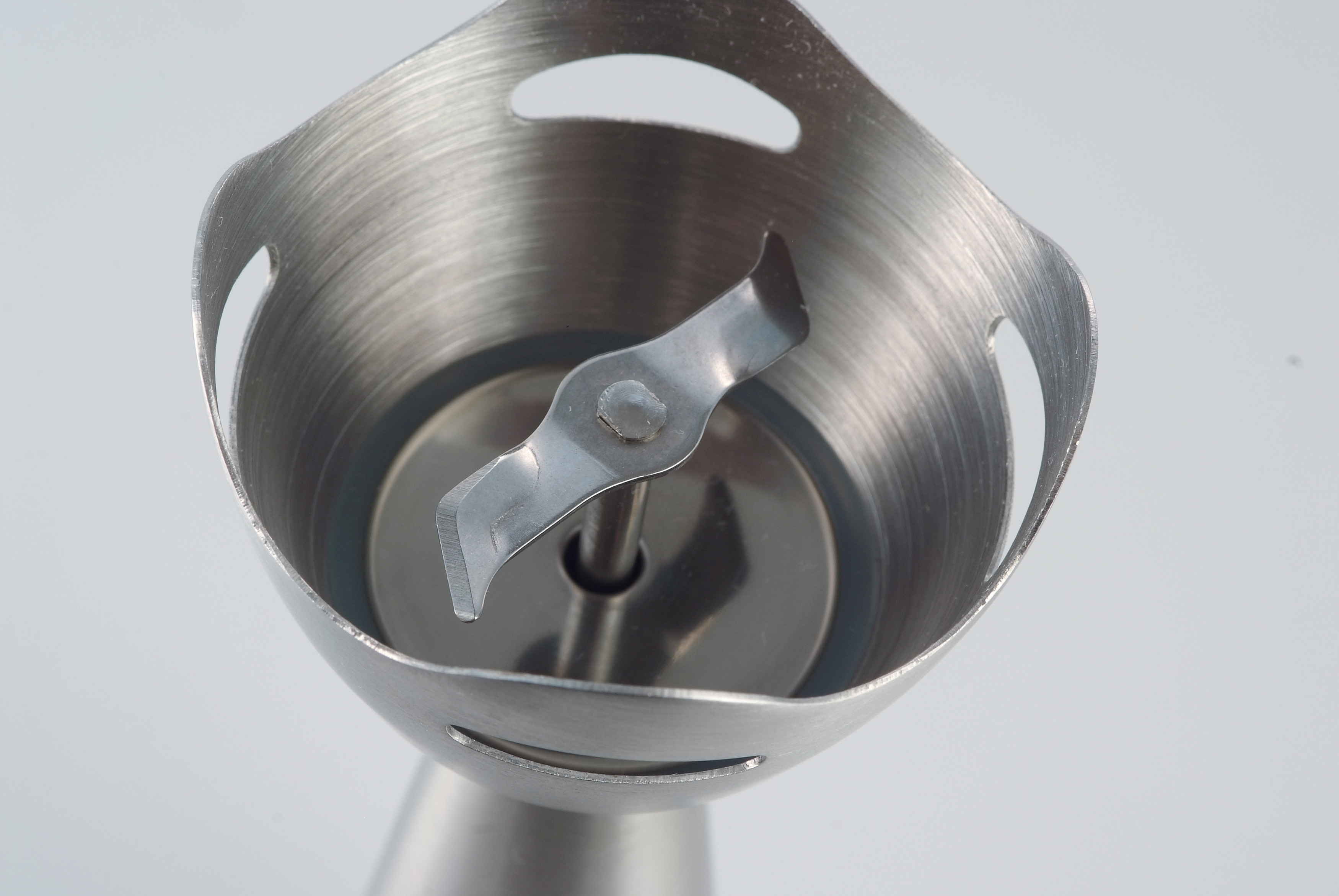 Primo piano di un accessorio per frullatore. Mostra una lama in acciaio inox all'interno di un alloggiamento metallico.