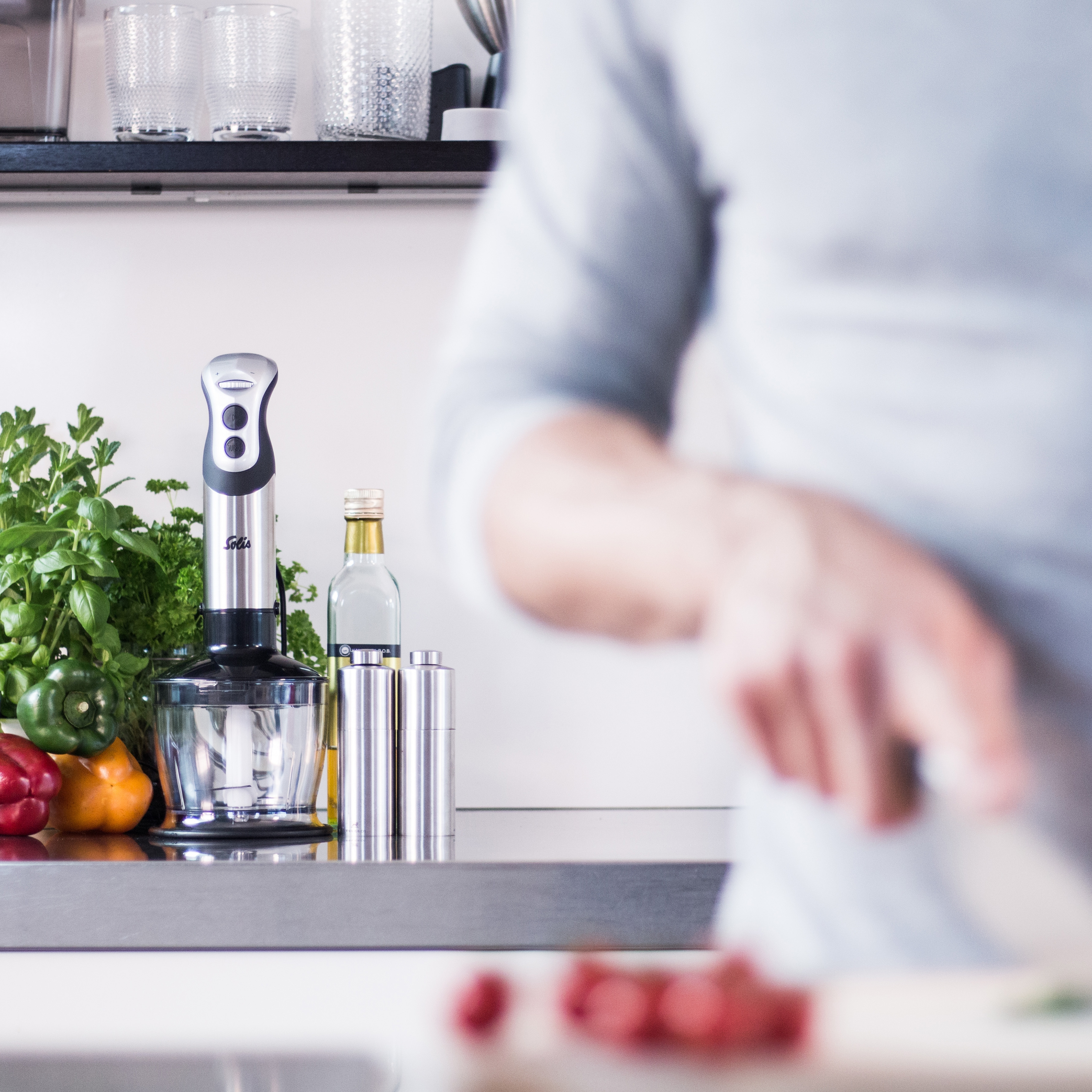 Una persona sta preparando gli ingredienti. Un frullatore, verdure e bottiglie sono su un bancone.