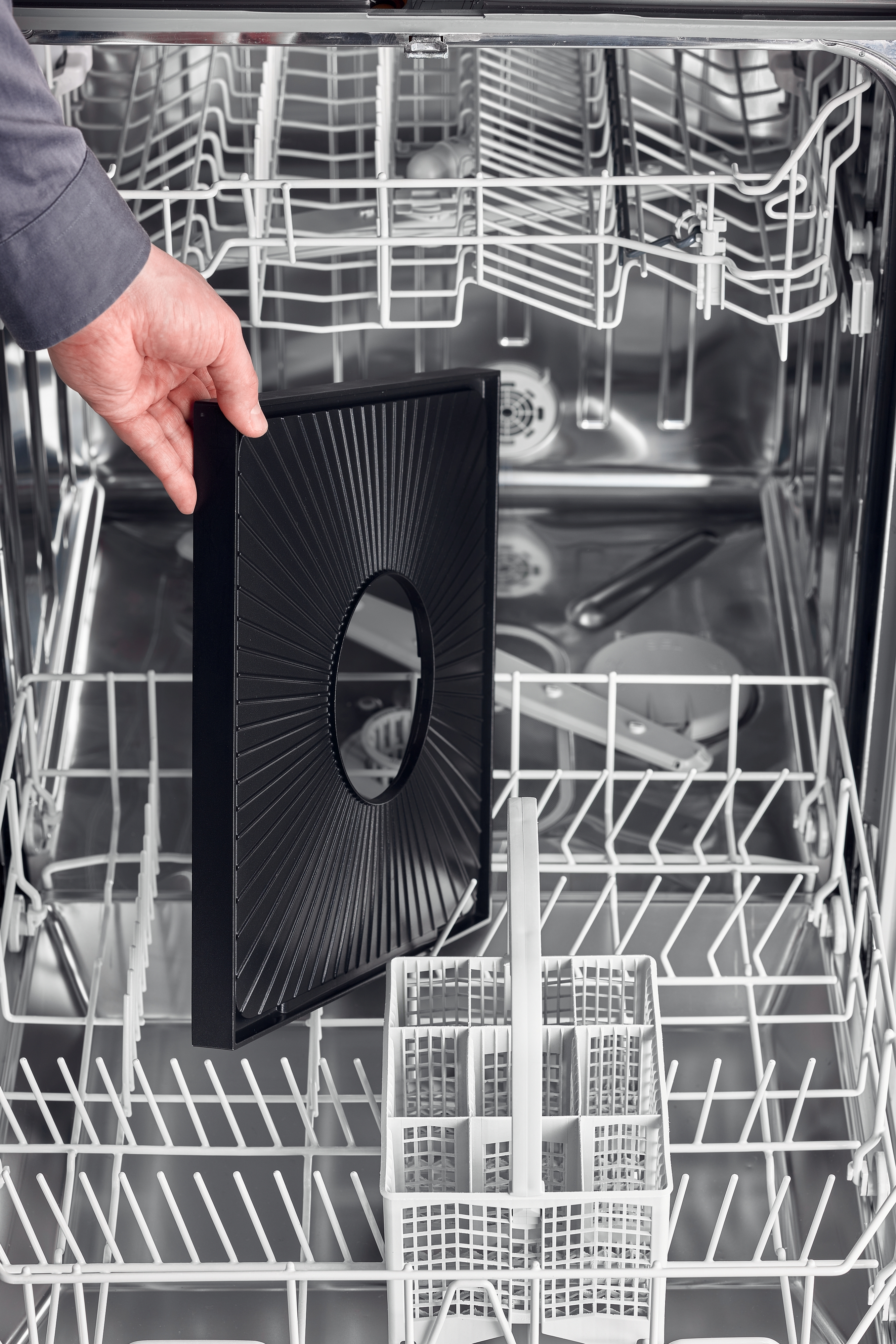 Ręka osoby wyjmująca filtr ze zmywarki.