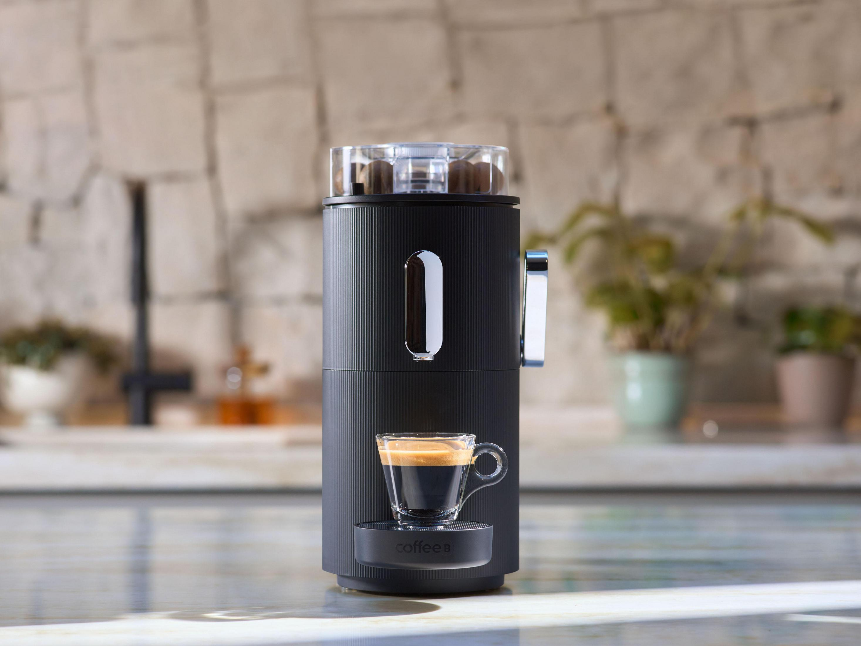 Schwarze Kaffeemaschine mit einer Glastasse Kaffee. Die Maschine hat eine Mühle und steht auf einer Arbeitsplatte.