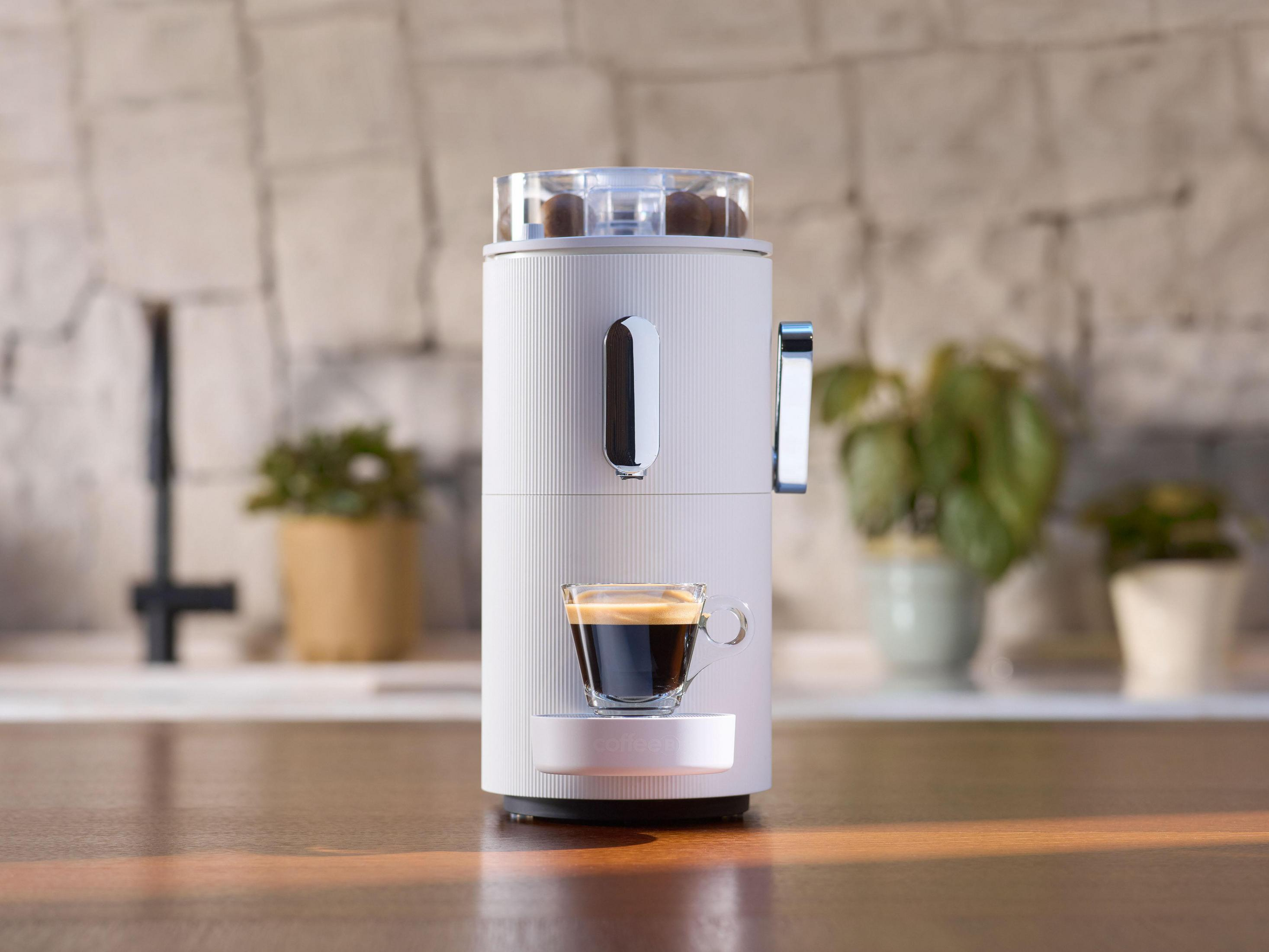 Weiße und graue Kaffeemaschine mit Kaffee in einem Glas. Mit Kaffeebohnenbehälter.