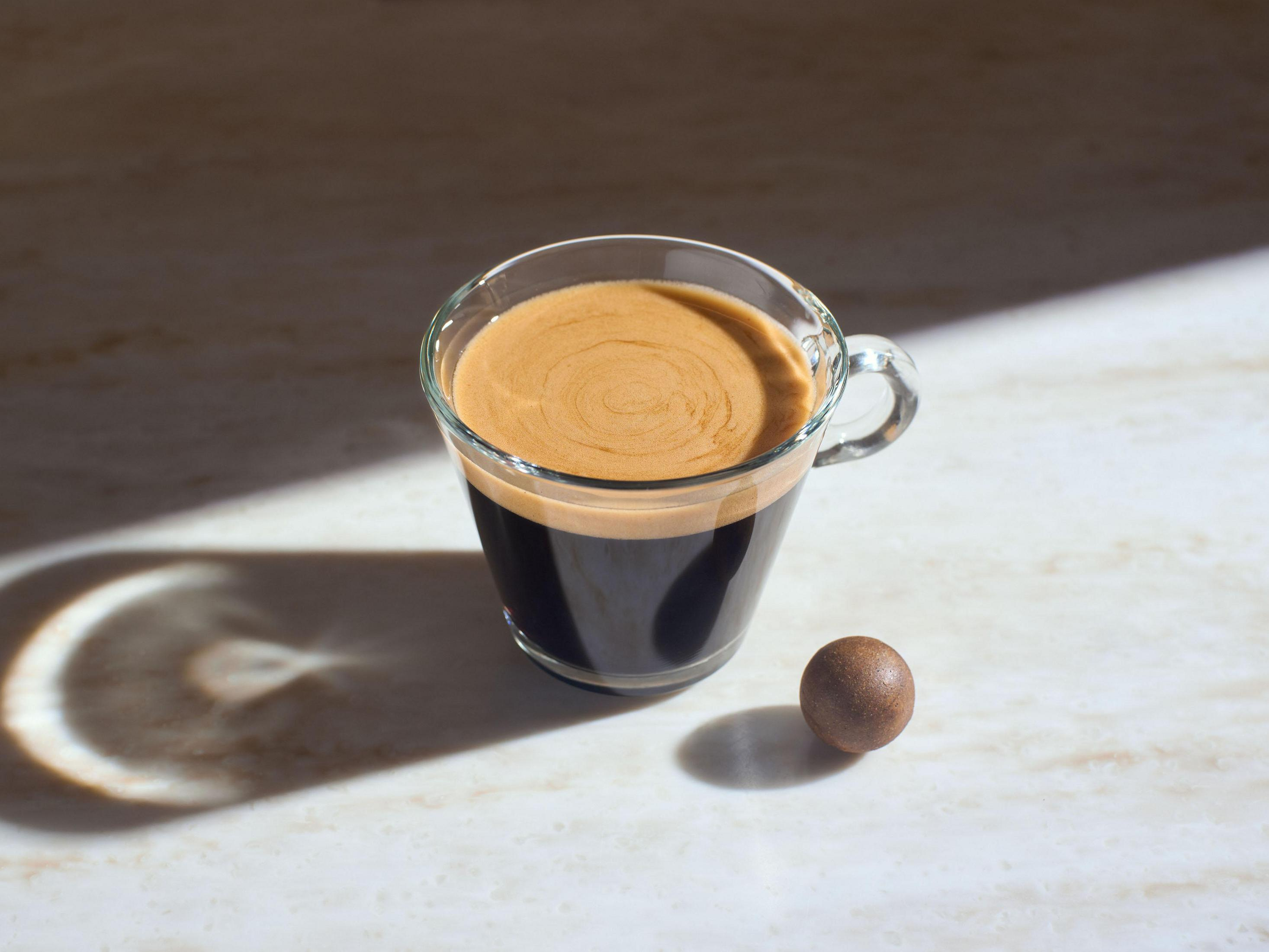 Una tazza di caffè con crema e una pallina di cioccolato su una superficie bianca.