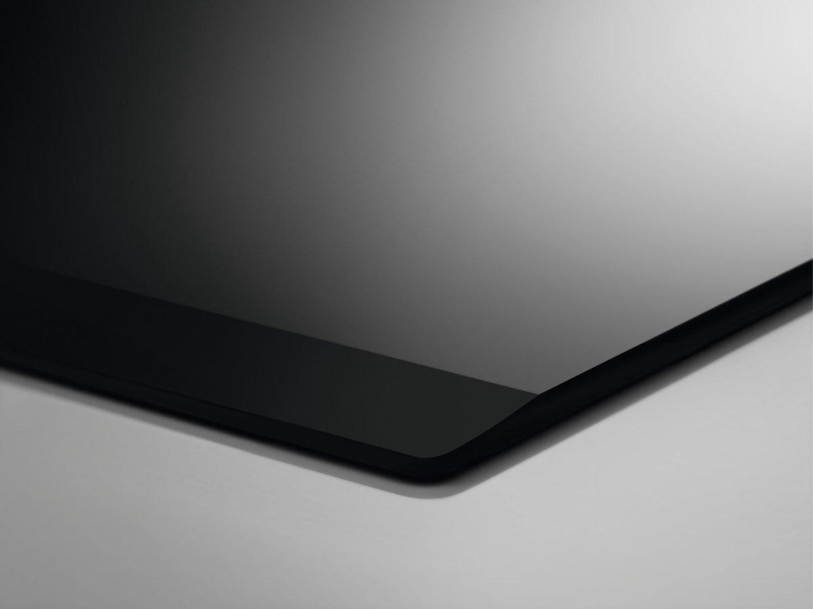 Czarna, błyszcząca powierzchnia, prawdopodobnie płyta grzewcza, na białym tle, zbliżenie.