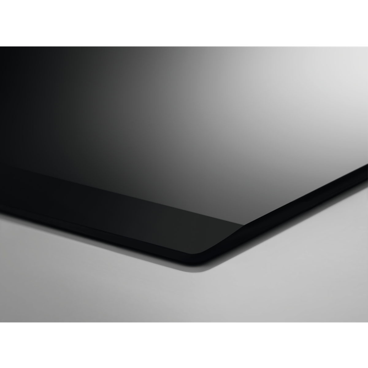 Zbliżenie czarnej, błyszczącej powierzchni, prawdopodobnie płyty grzewczej, z odbiciem światła.