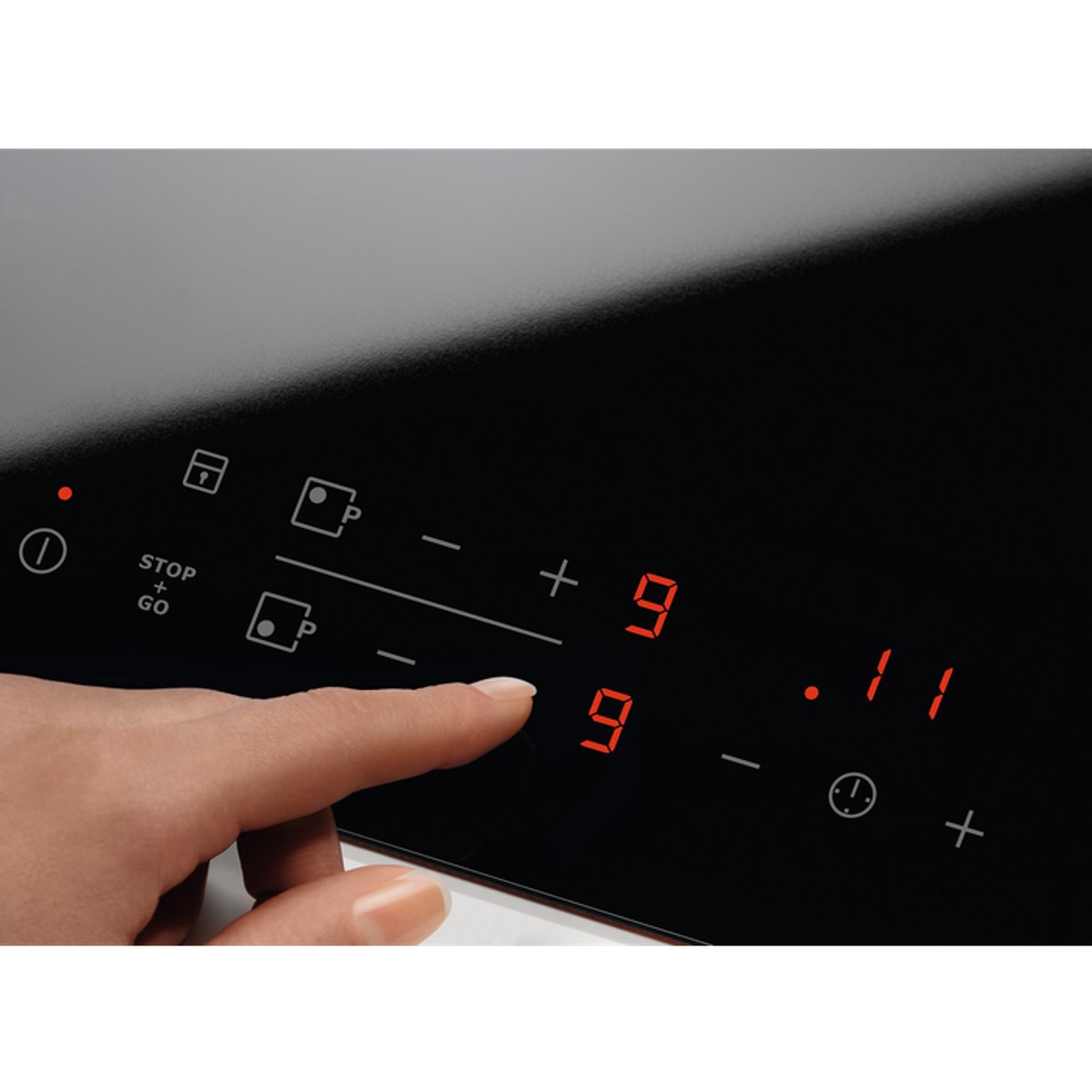 Ręka naciska przycisk na czarnej płycie kuchennej, wyświetlając cyfrę 9. Widoczne są czerwone cyfry.